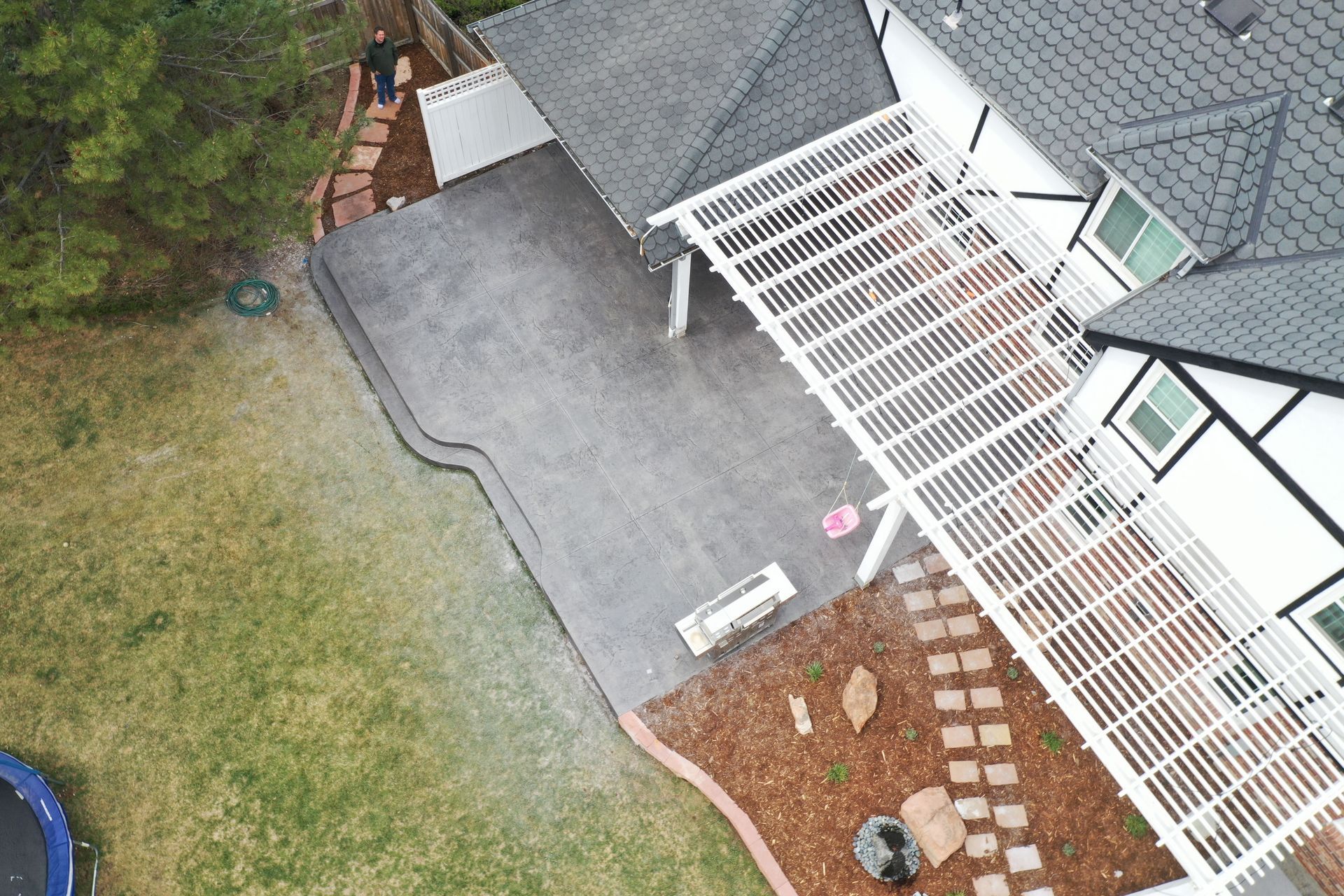 Overhead view of a house with a gray deck, white pergola, and landscaping.