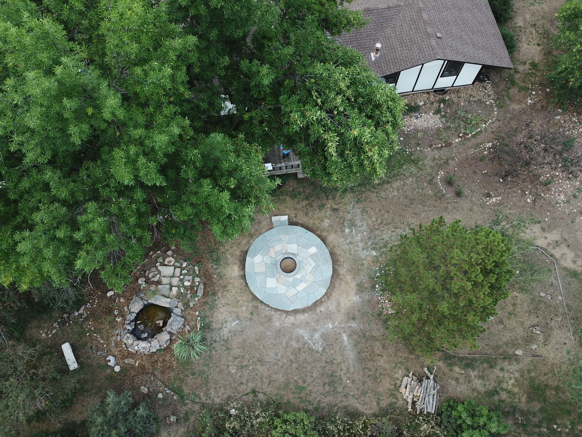 Overhead view of a stone circular structure with a hole in the center, next to a building and trees.
