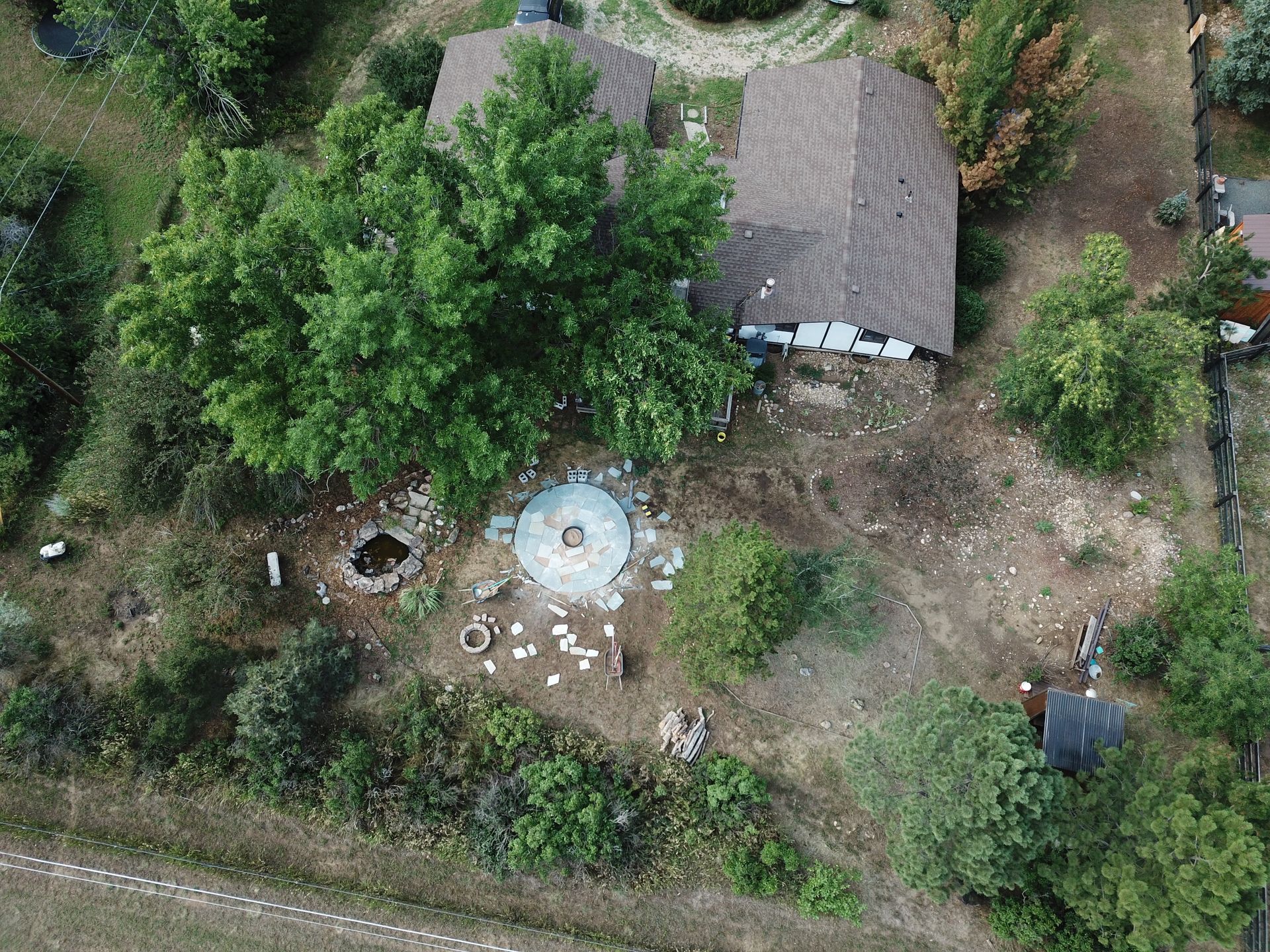 Aerial view of a home with a brown roof and a circular structure in the yard, surrounded by trees and vegetation.