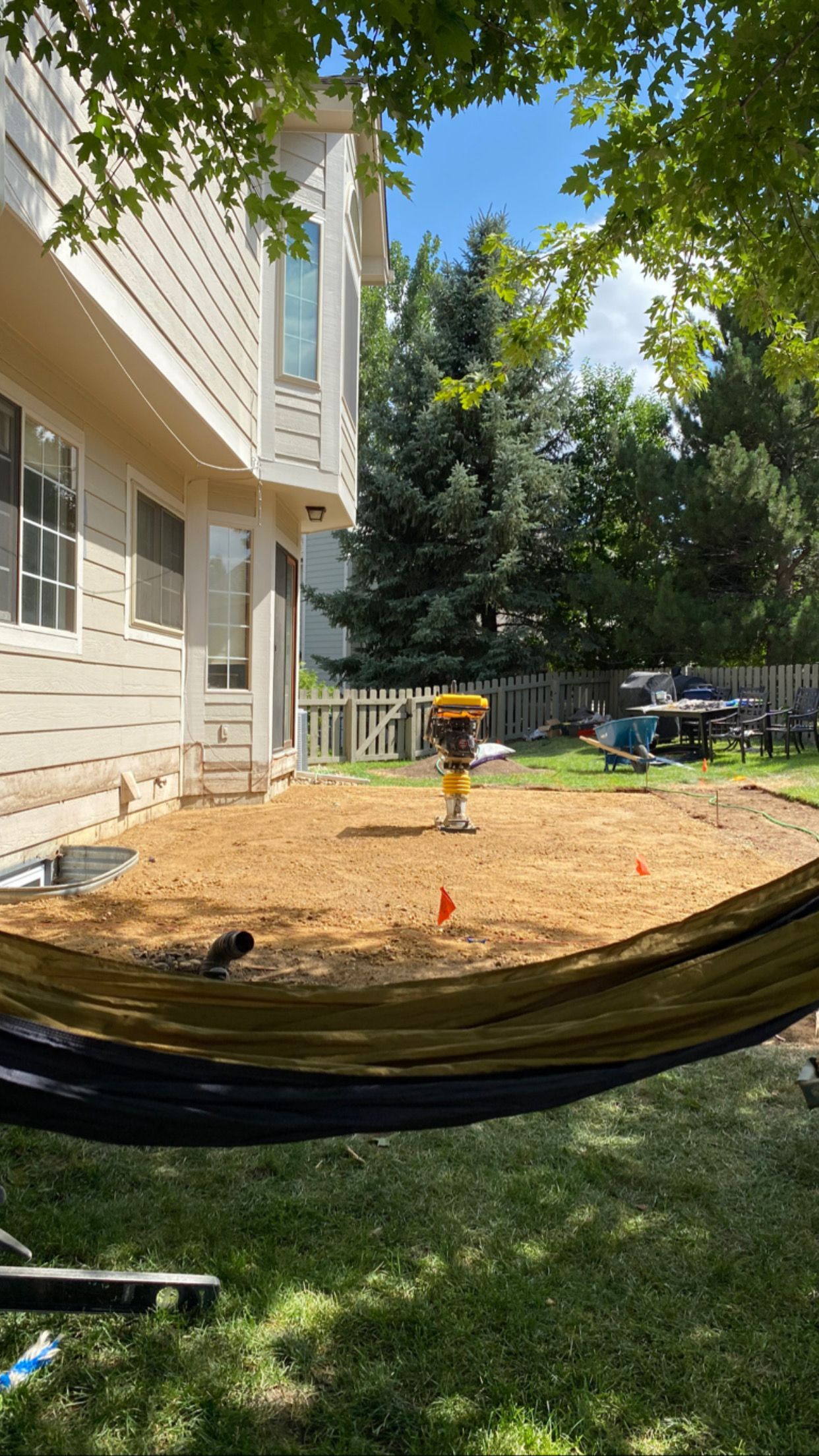 A backyard with a construction area, a hammock, and a house. Construction tool compacting soil.