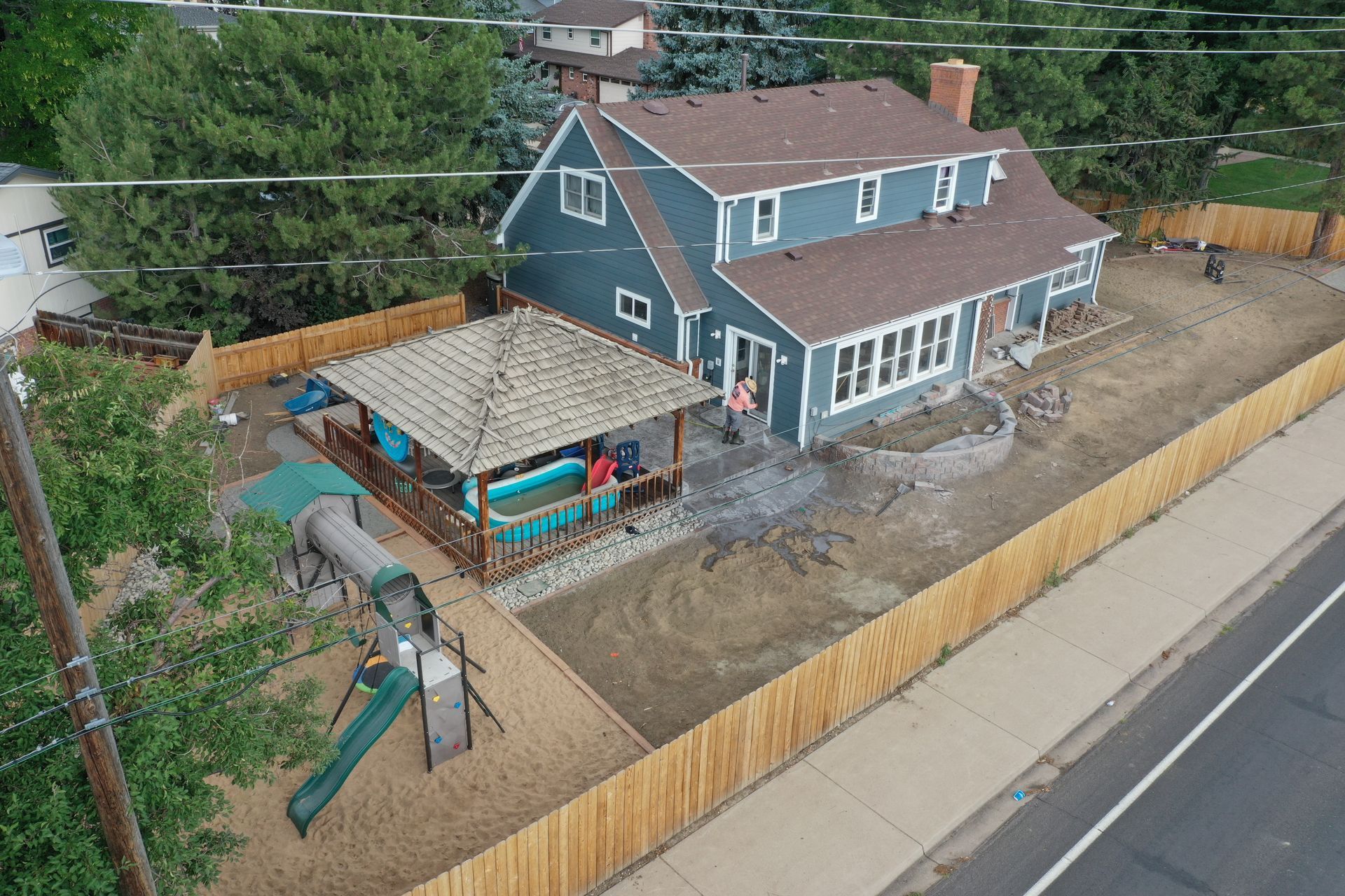Blue house with wooden fence, patio, hot tub, and playground.