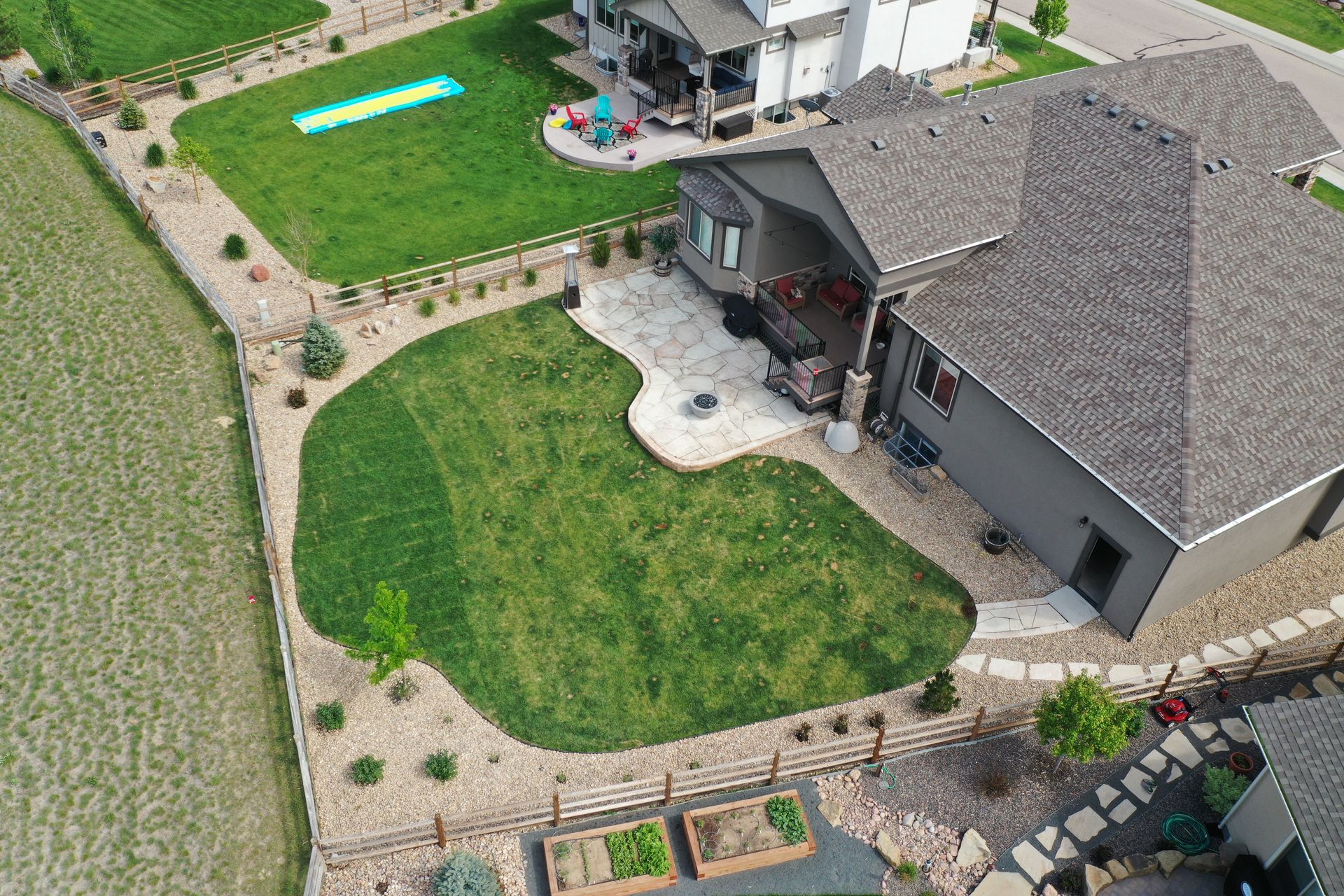Aerial view of a house with a green lawn, stone patio, and wooden fence in a suburban setting.