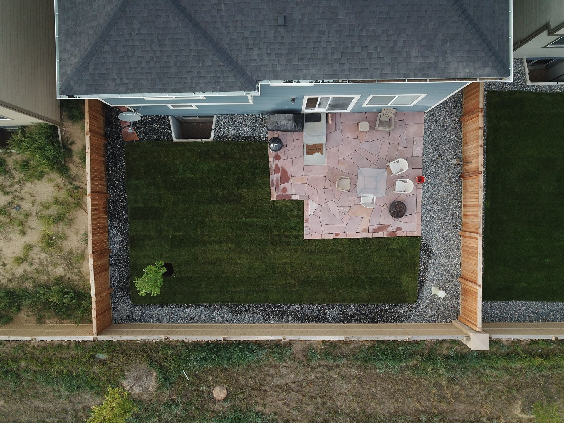 Overhead view of a backyard with a patio, lawn, and wooden fence.