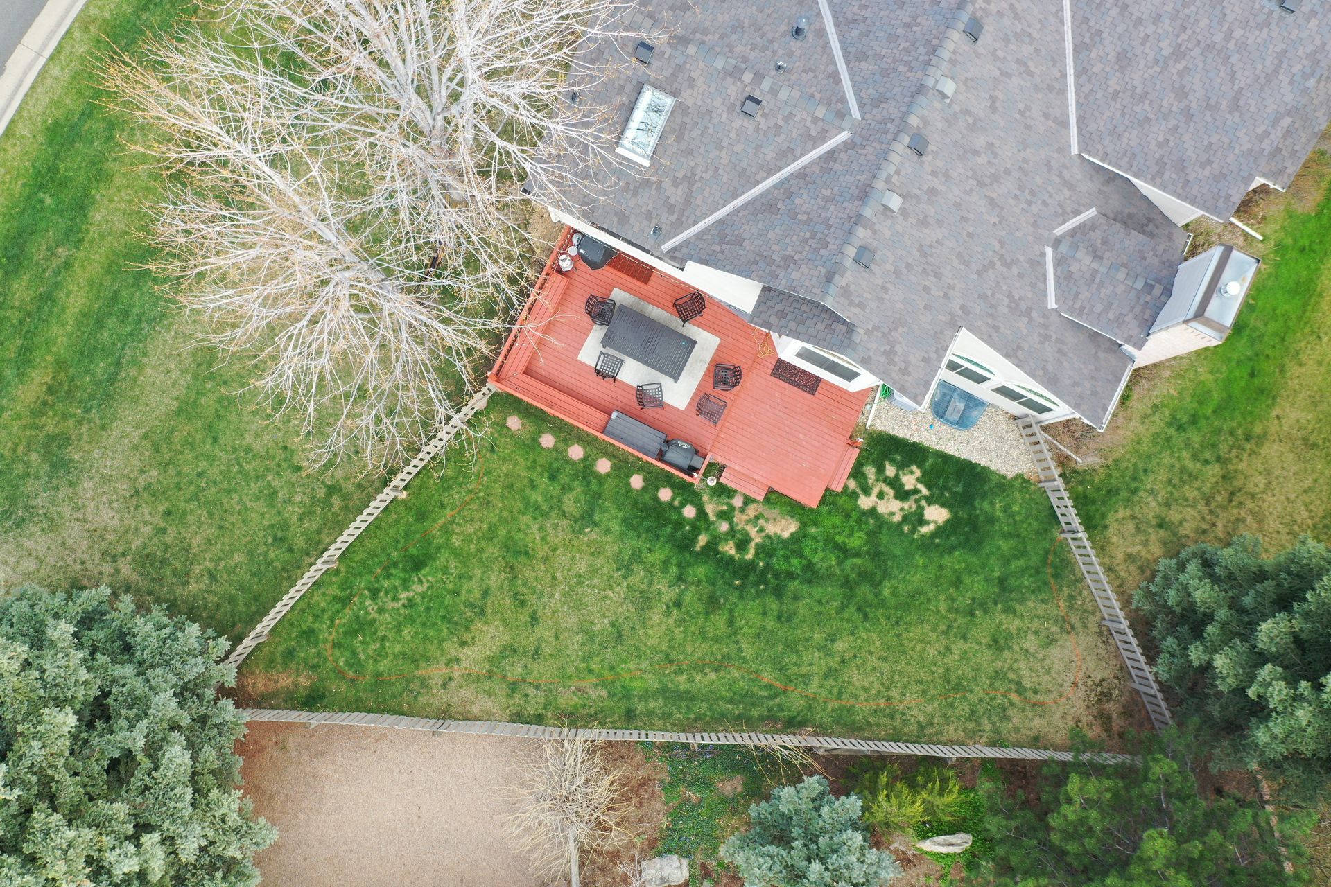 Overhead view of a house with a red deck and green lawn. A leafless tree stands beside the deck.