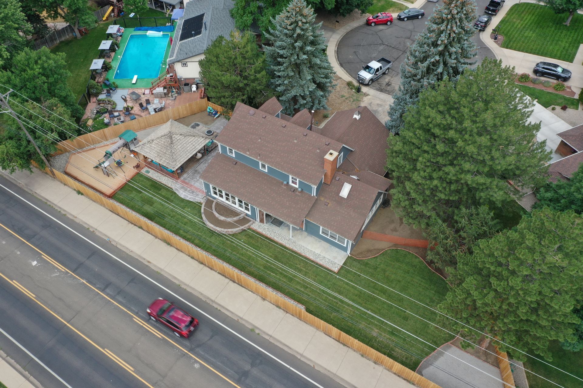 Aerial view of a blue house with a pool, backyard deck, and road with a car.