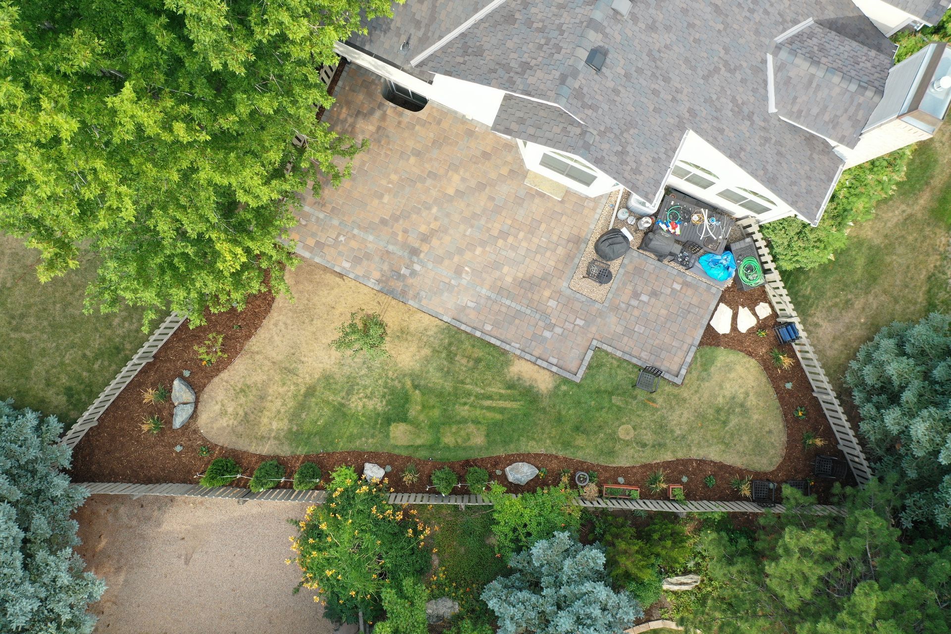 Aerial view of a house with a landscaped yard, stone patio, green grass, and trees.