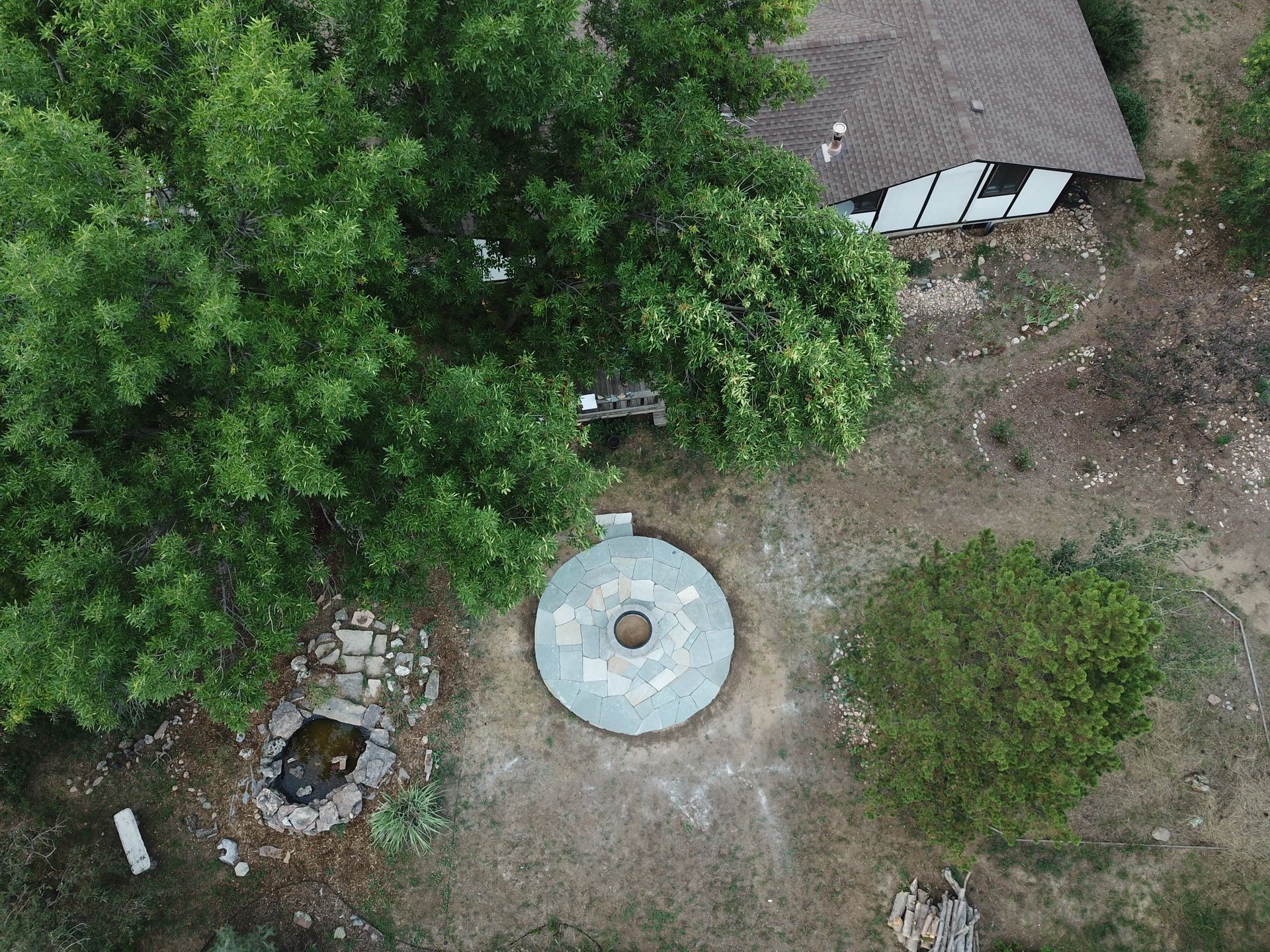 Overhead view of a circular stone structure, possibly a well, next to a house and trees.