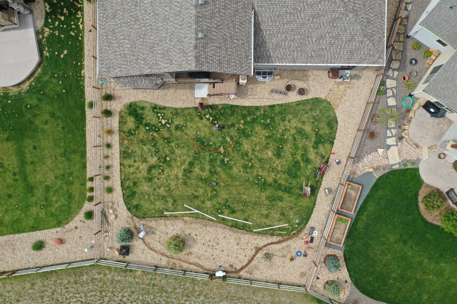Aerial view of a backyard with a house, green lawn, rock pathways, and landscaping features.