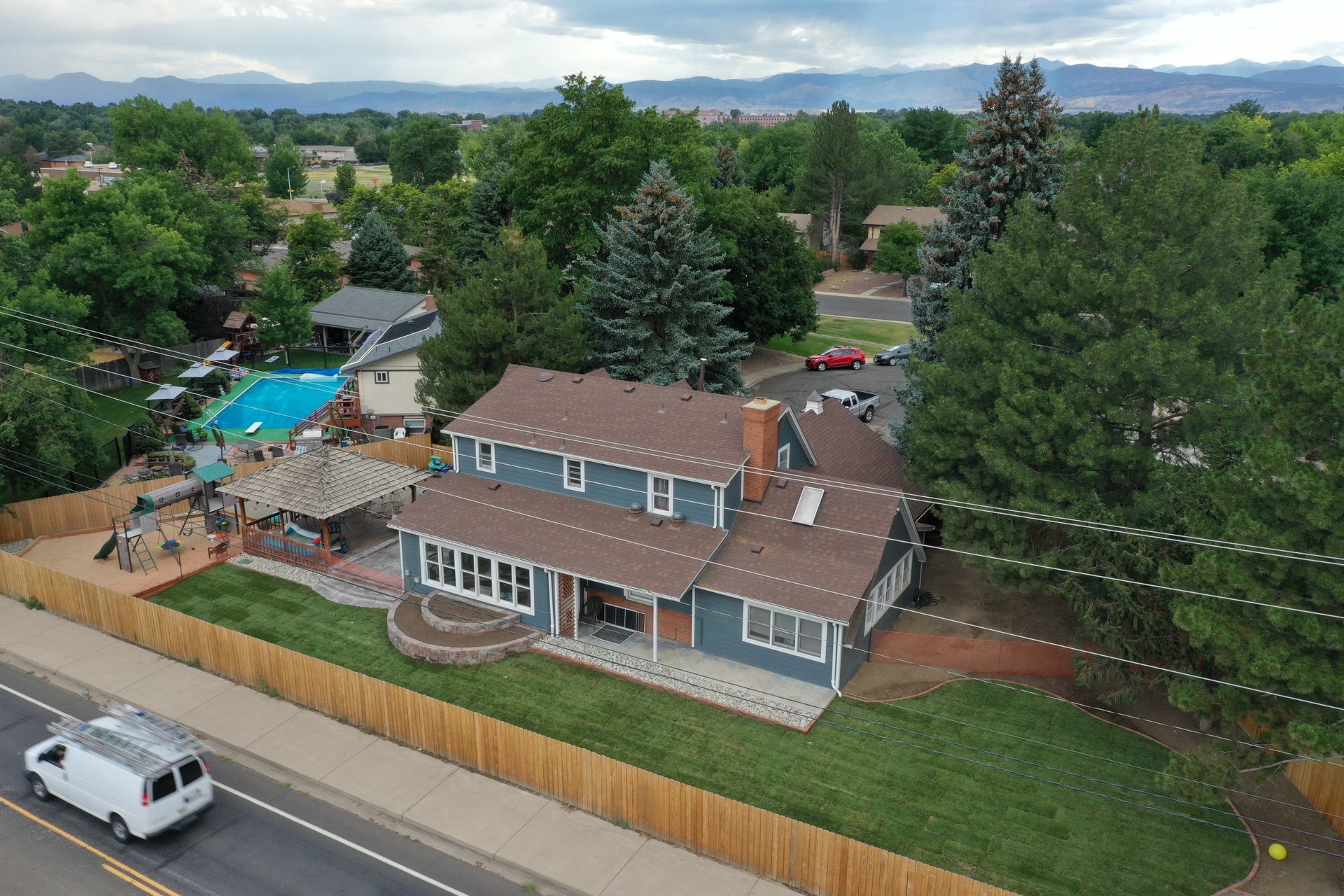 Aerial view of a blue house with a brown roof and a pool in the backyard.