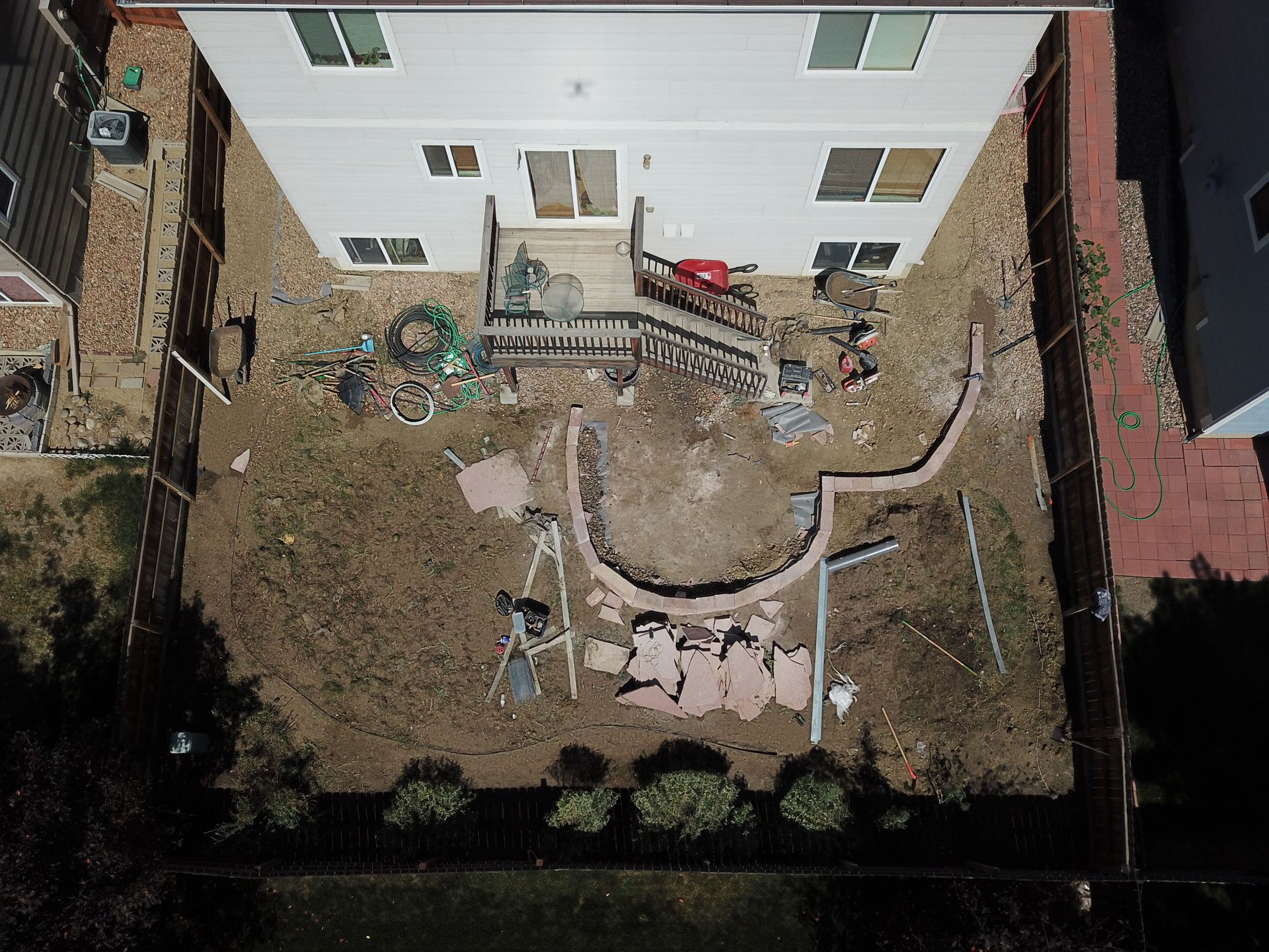 Aerial view of a backyard undergoing landscaping. Dirt, stone, and debris surround a house with a wooden deck.