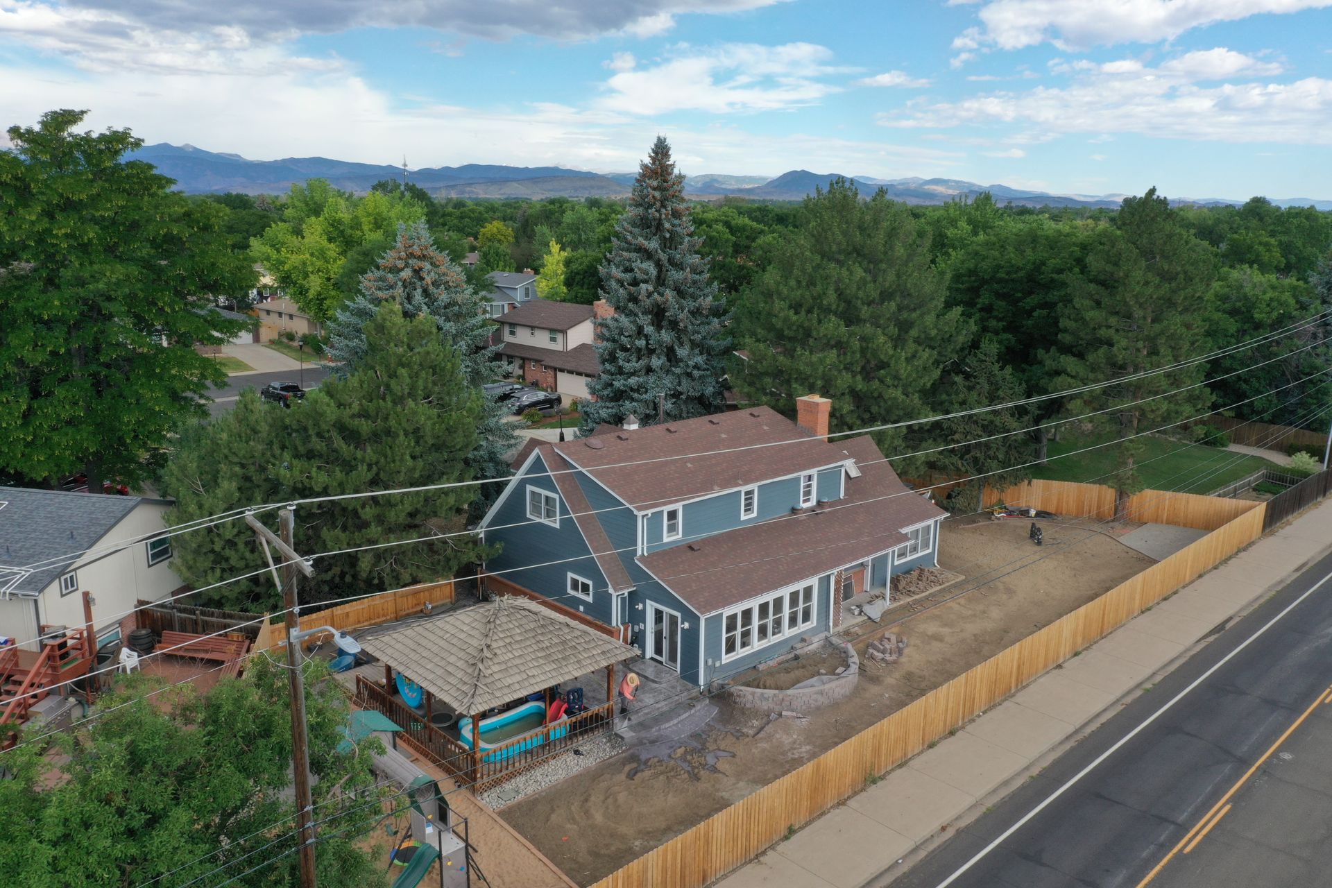 Aerial view of a blue two-story house with a brown roof and a wooden fence along a road.