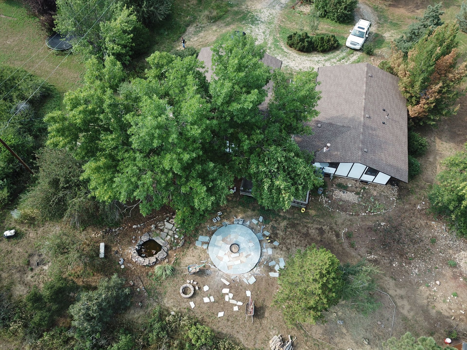 Overhead view of a house with a stone patio, pond, and large tree. A car is parked nearby.