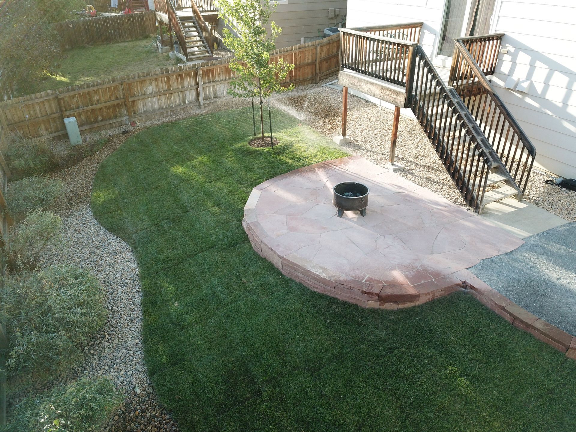 Backyard with a lawn, a stone patio with a fire pit, and a wooden deck.