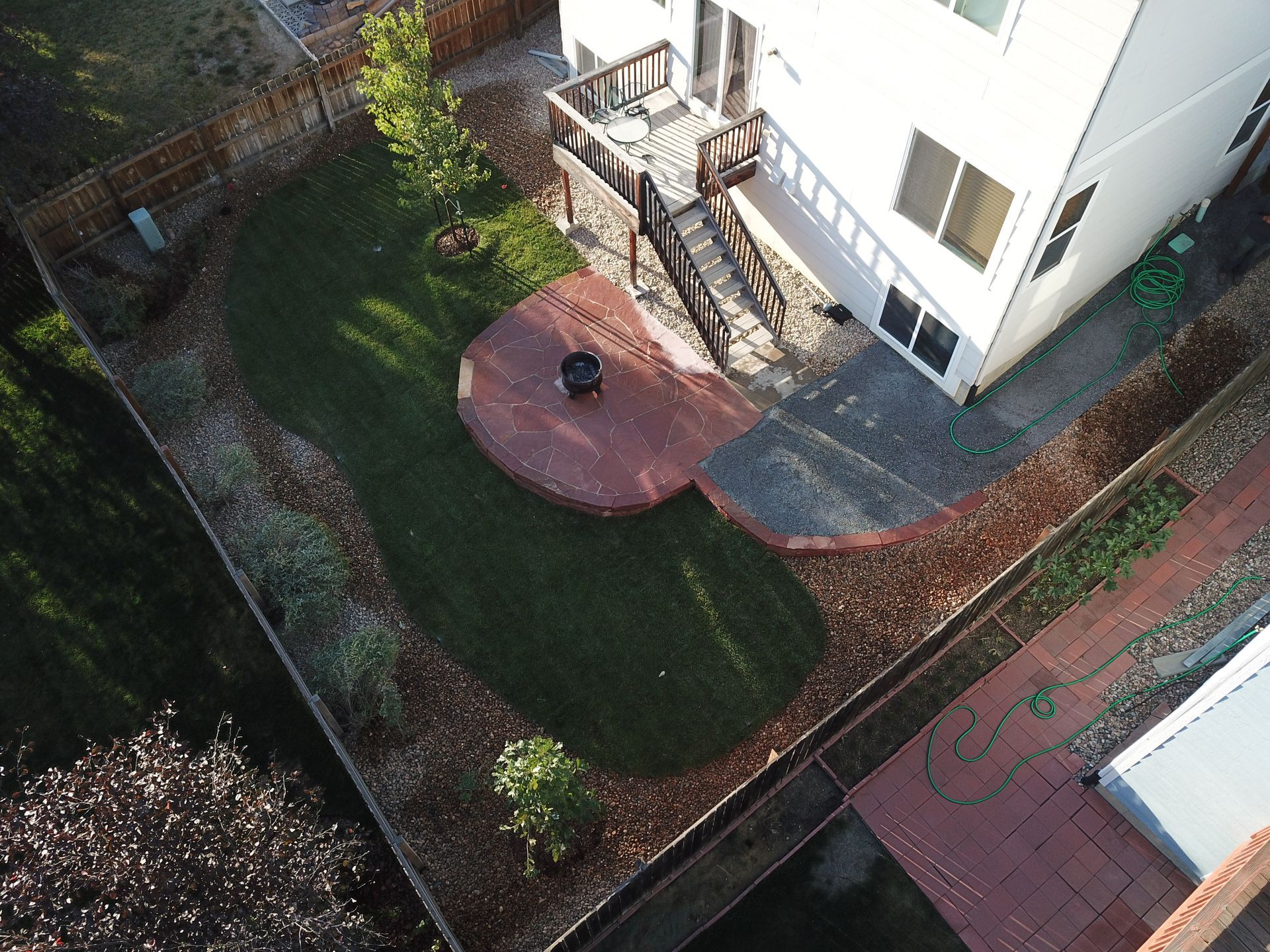 Overhead view of a house with backyard; deck, green lawn, red brick patio, and wooden fence.