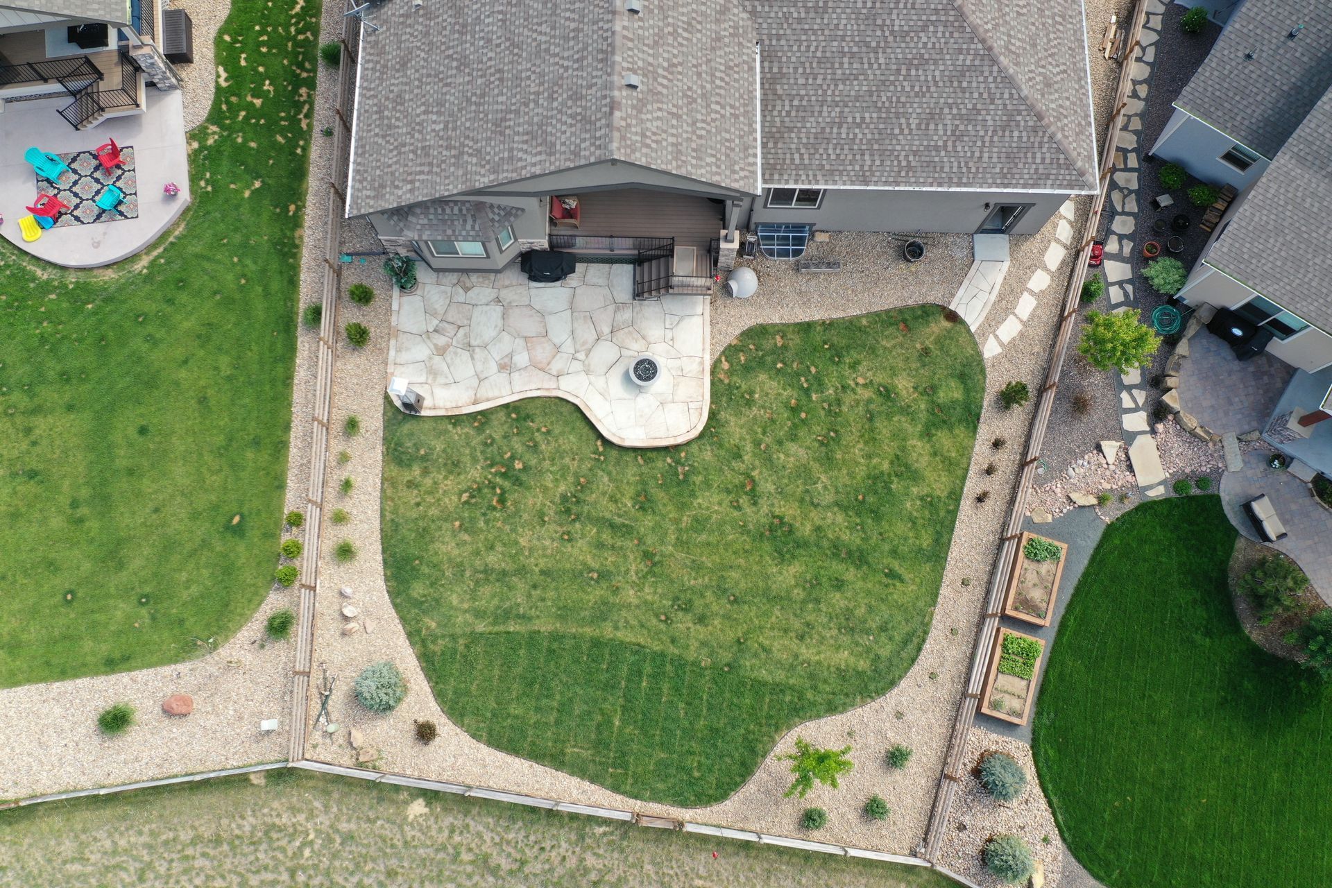 Overhead view of a house with a stone patio, fire pit, and a green lawn bordered by landscaping.