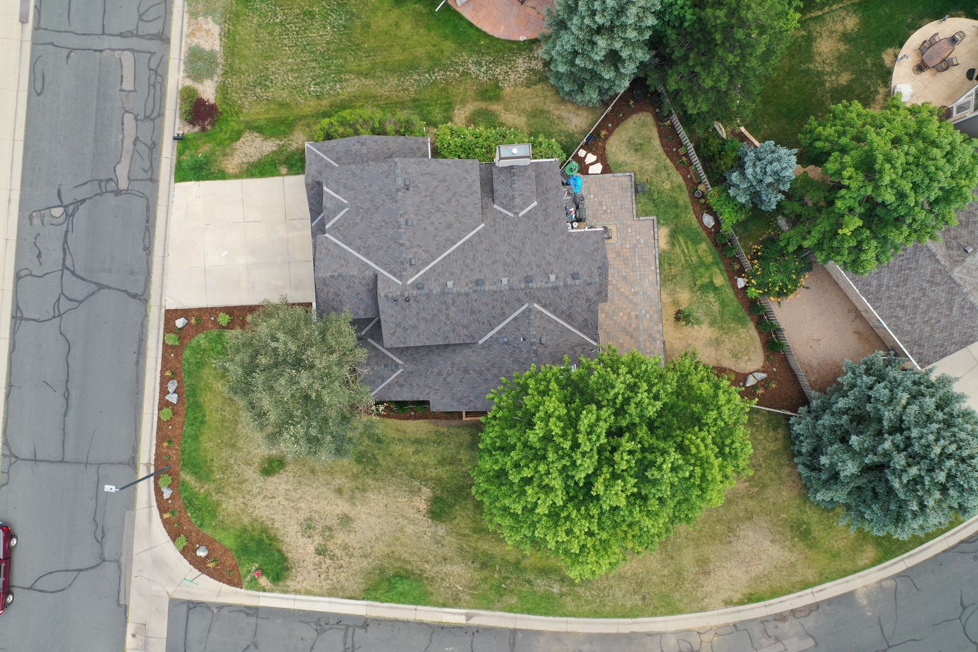 Overhead view of a house with a dark gray roof, surrounded by trees and landscaping.