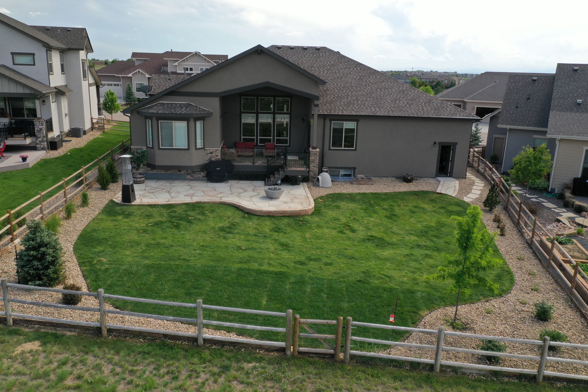 Backyard view of a brown house with green lawn, stone patio, and wooden fence.