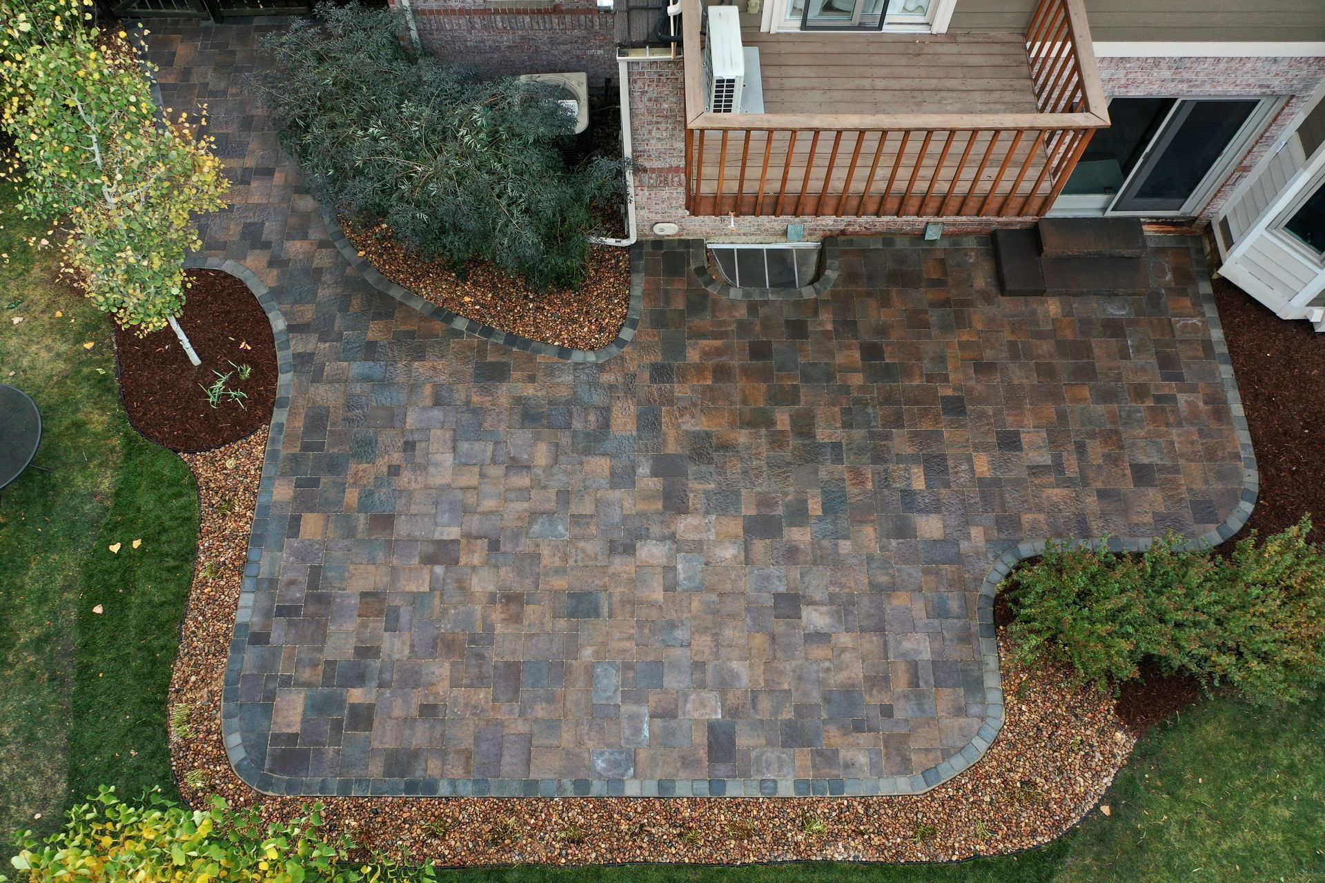 Overhead view of a brick patio with a deck, surrounded by landscaping, mulch, and grass.