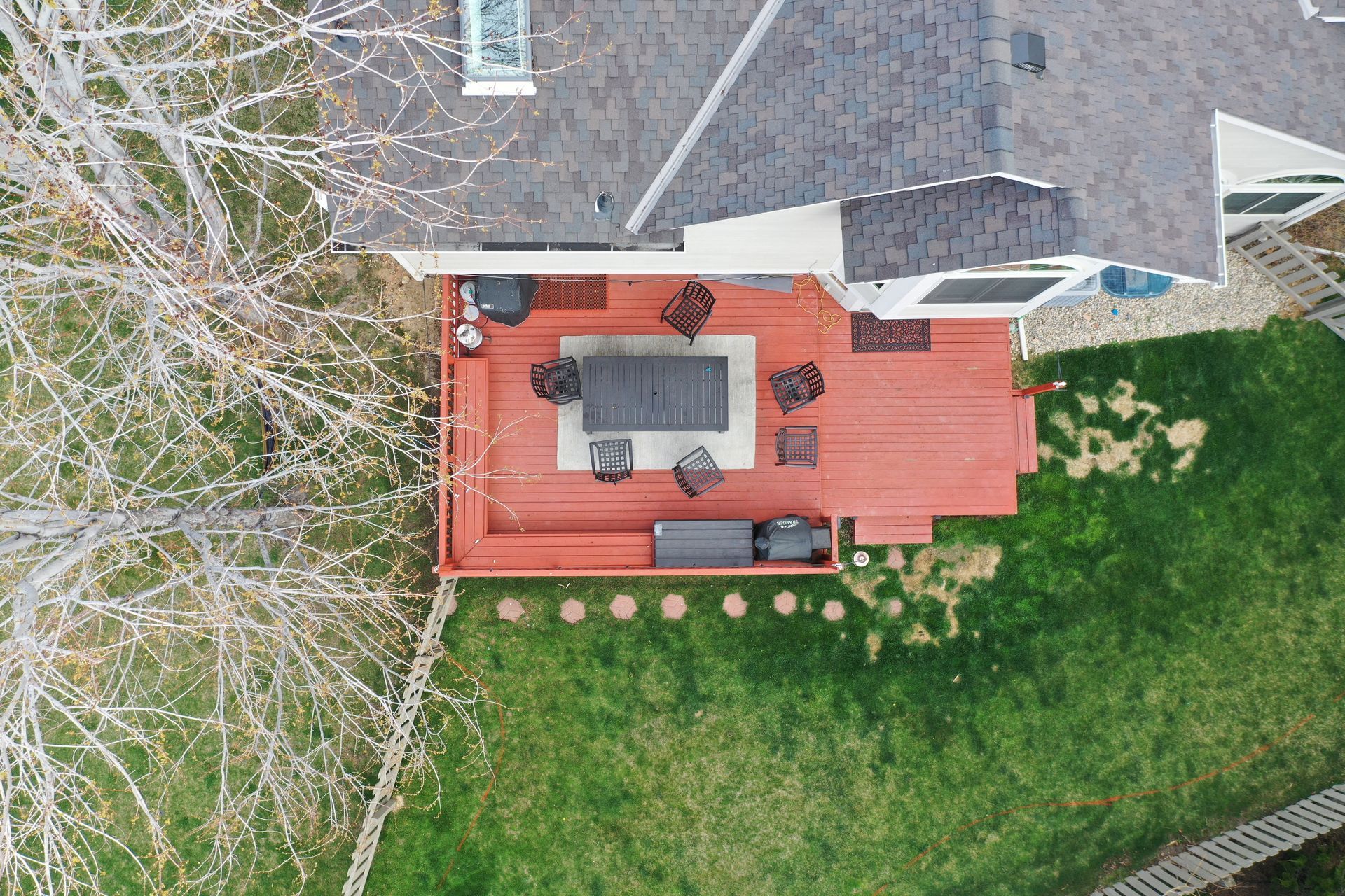 Overhead view of a house with a red deck and lawn, furnished with patio furniture.