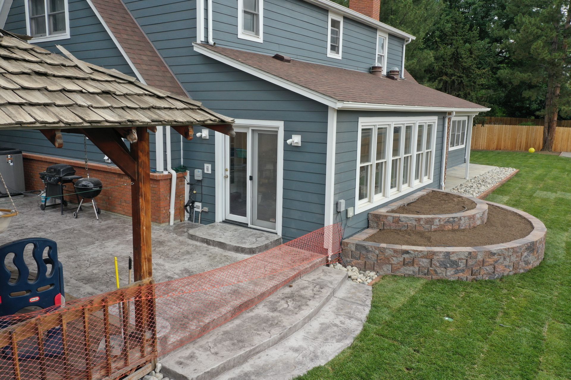 A two-story blue house with a deck and tiered stone planters in the yard.