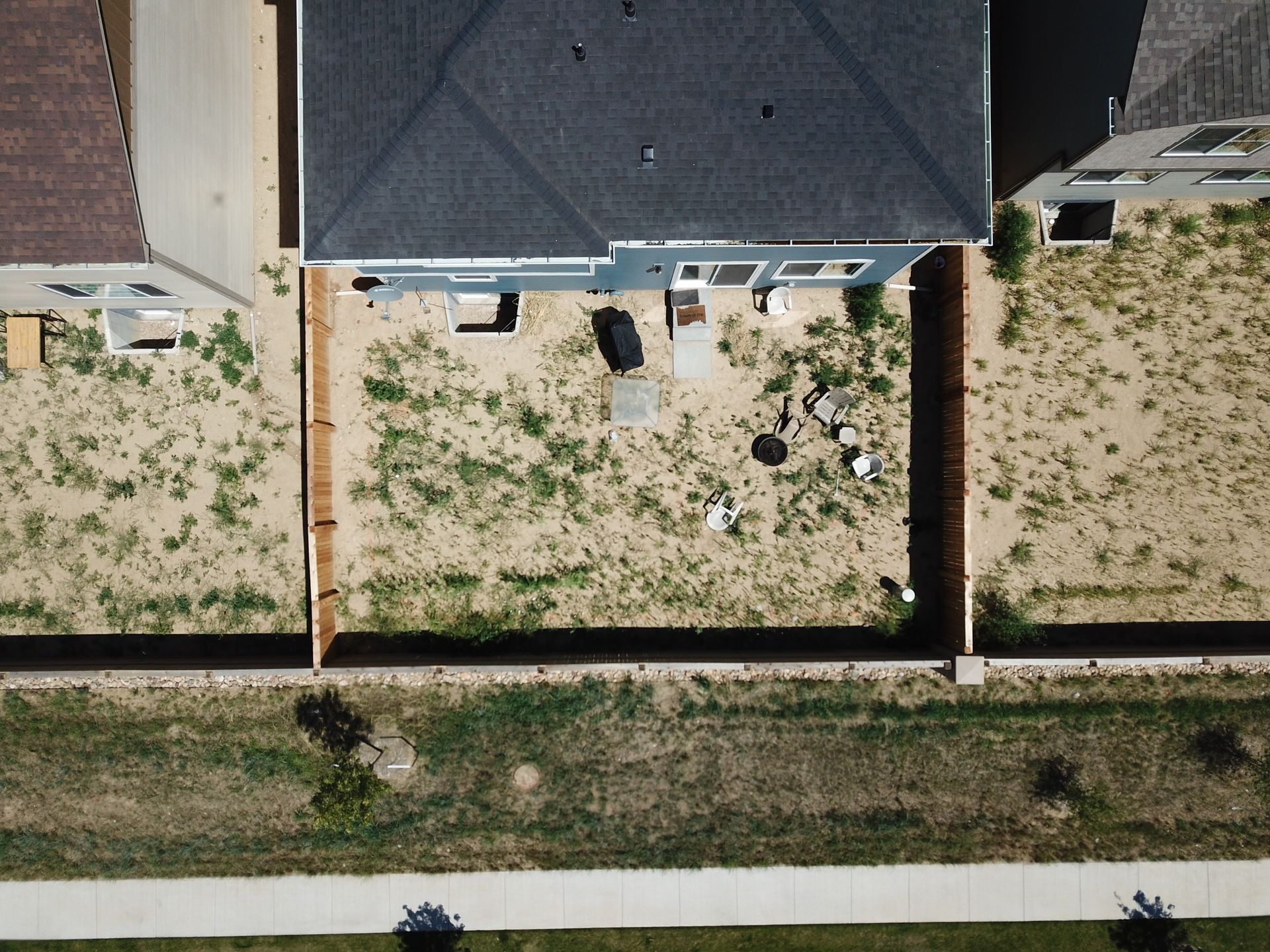 Overhead view of a house with a blue exterior and brown yard, surrounded by fences.