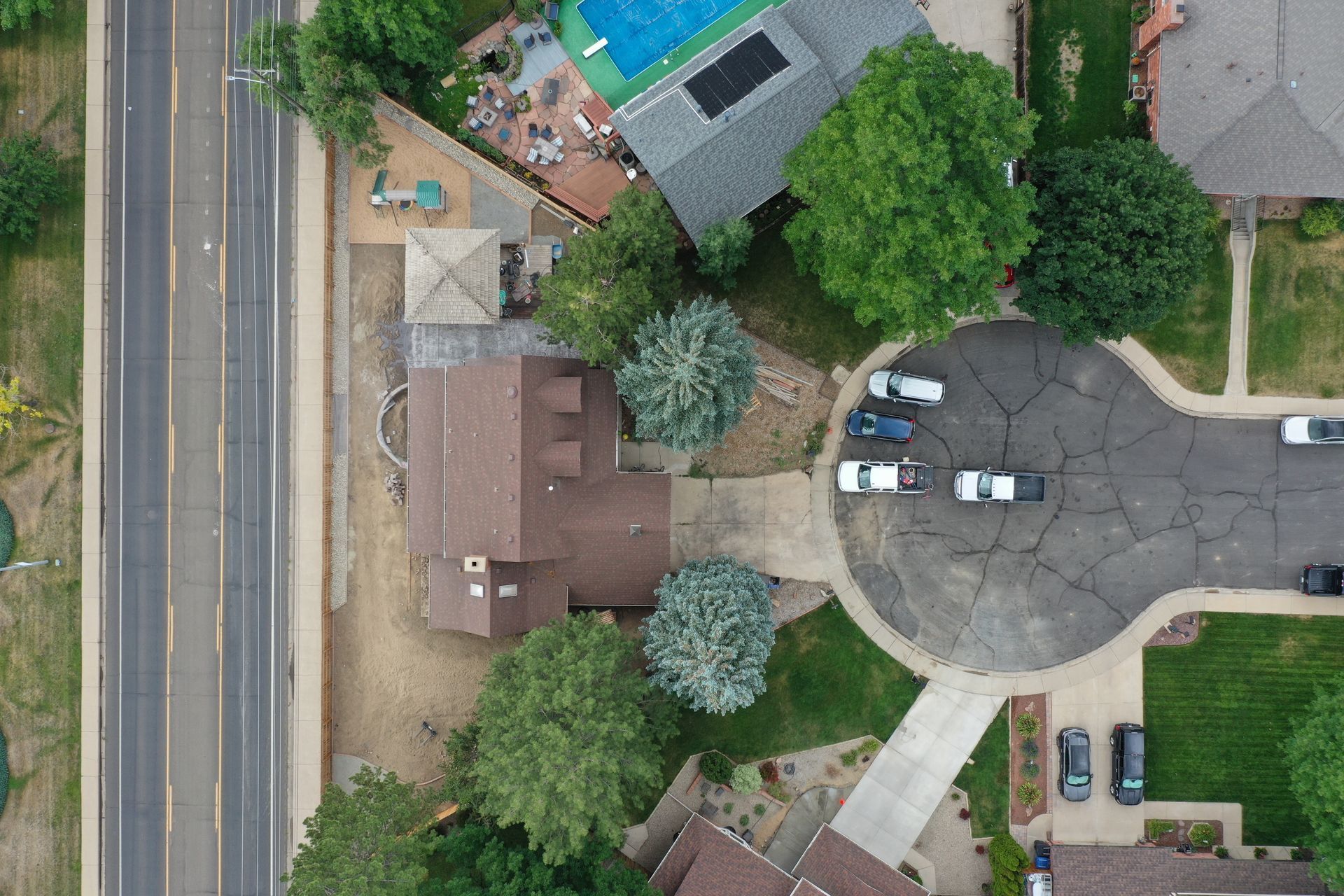Aerial view of a suburban house with a driveway full of cars, next to a road.