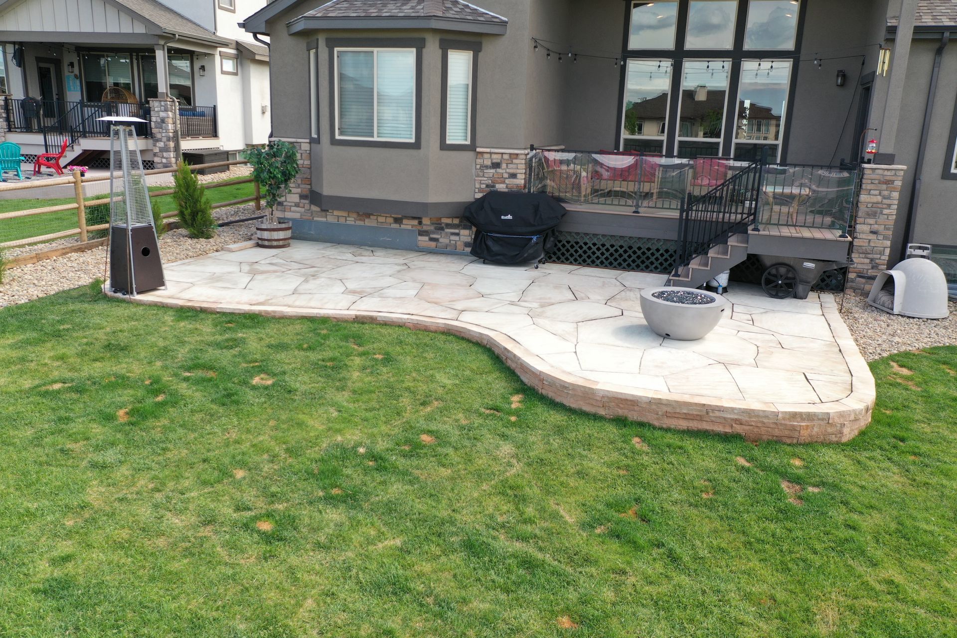 Backyard patio with stone pavers, grass, a fire pit, and a house.