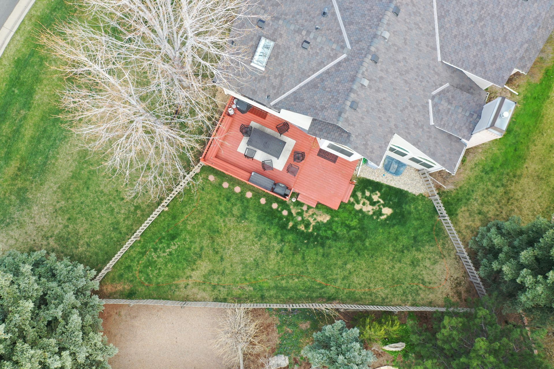 Aerial view of a home with a red deck and green lawn surrounded by trees and a stone wall.