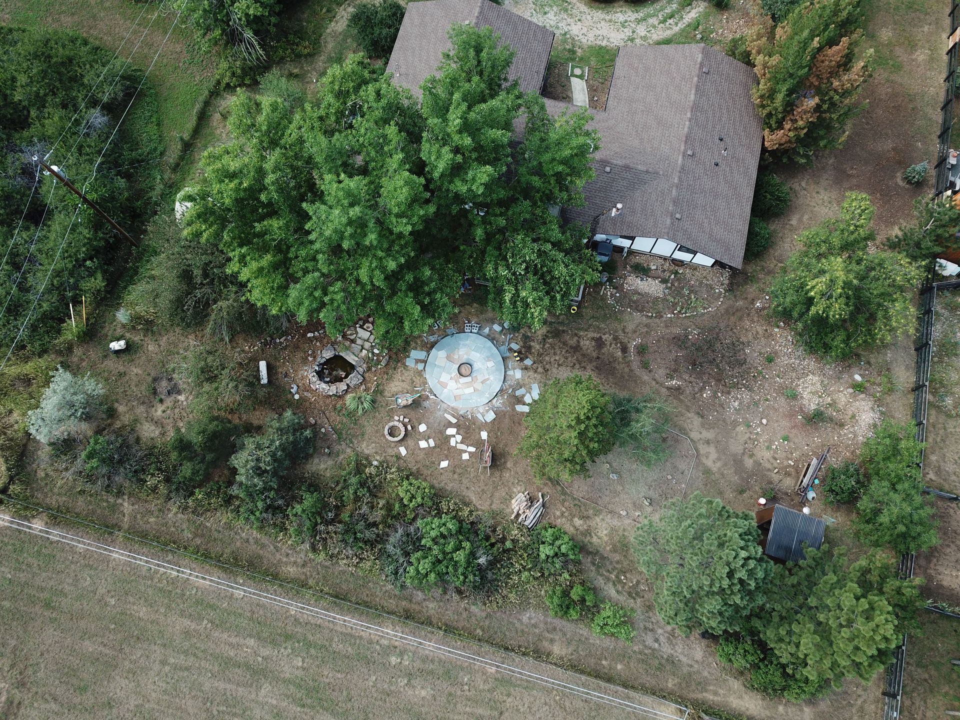 Aerial view of a house surrounded by trees and a circular stone structure in the yard, near farmland.