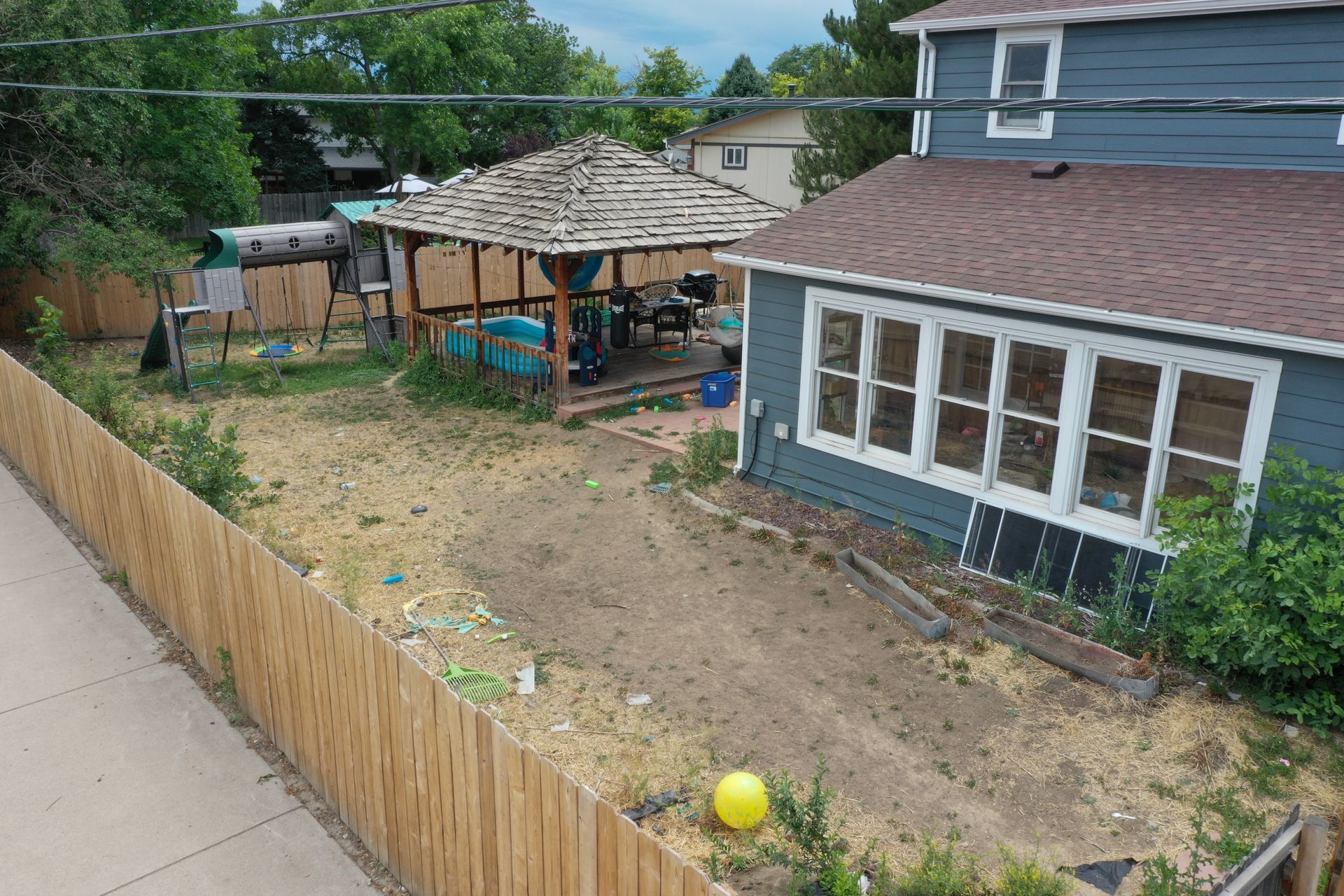 Backyard with a wooden fence, gazebo, blue house, and yellow ball.