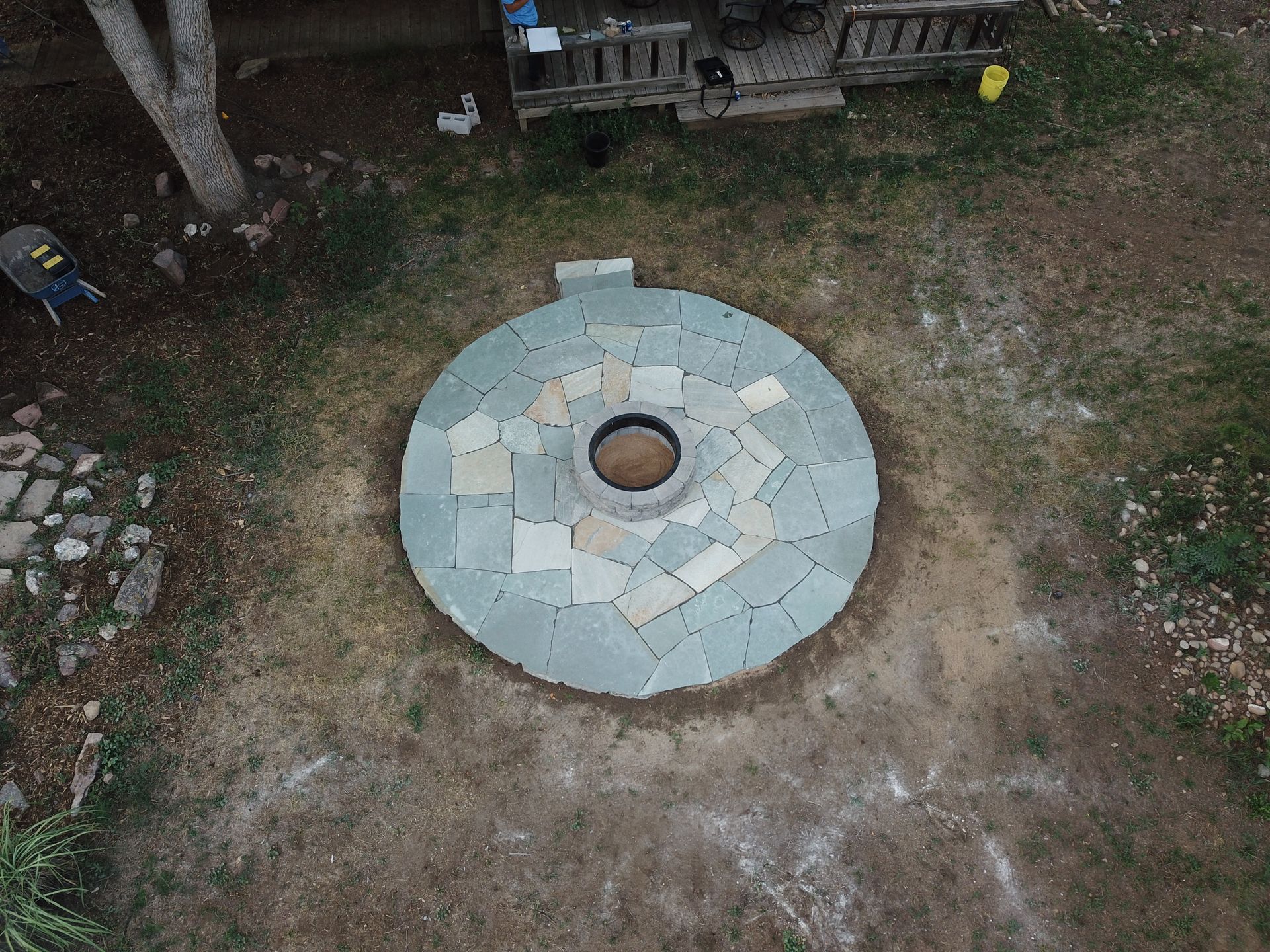 Aerial view of a circular stone patio with a central fire pit, in a grassy backyard.