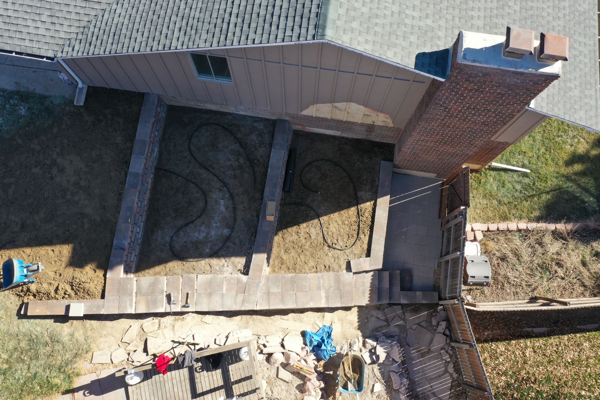 Overhead view of backyard with brick features and a chimney, dry grass, and construction materials.