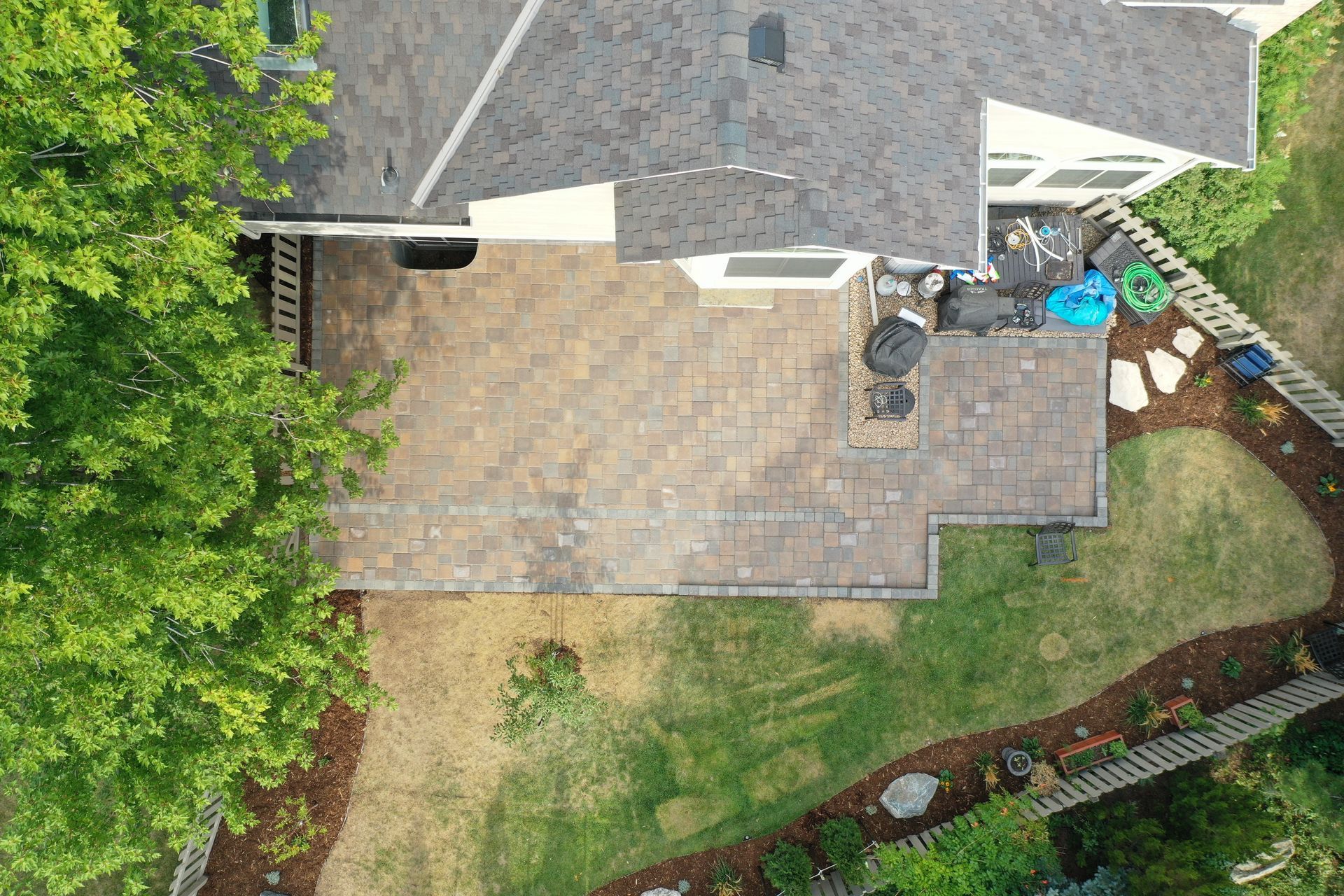 Overhead view of a house with a stone patio, lawn, and surrounding greenery.