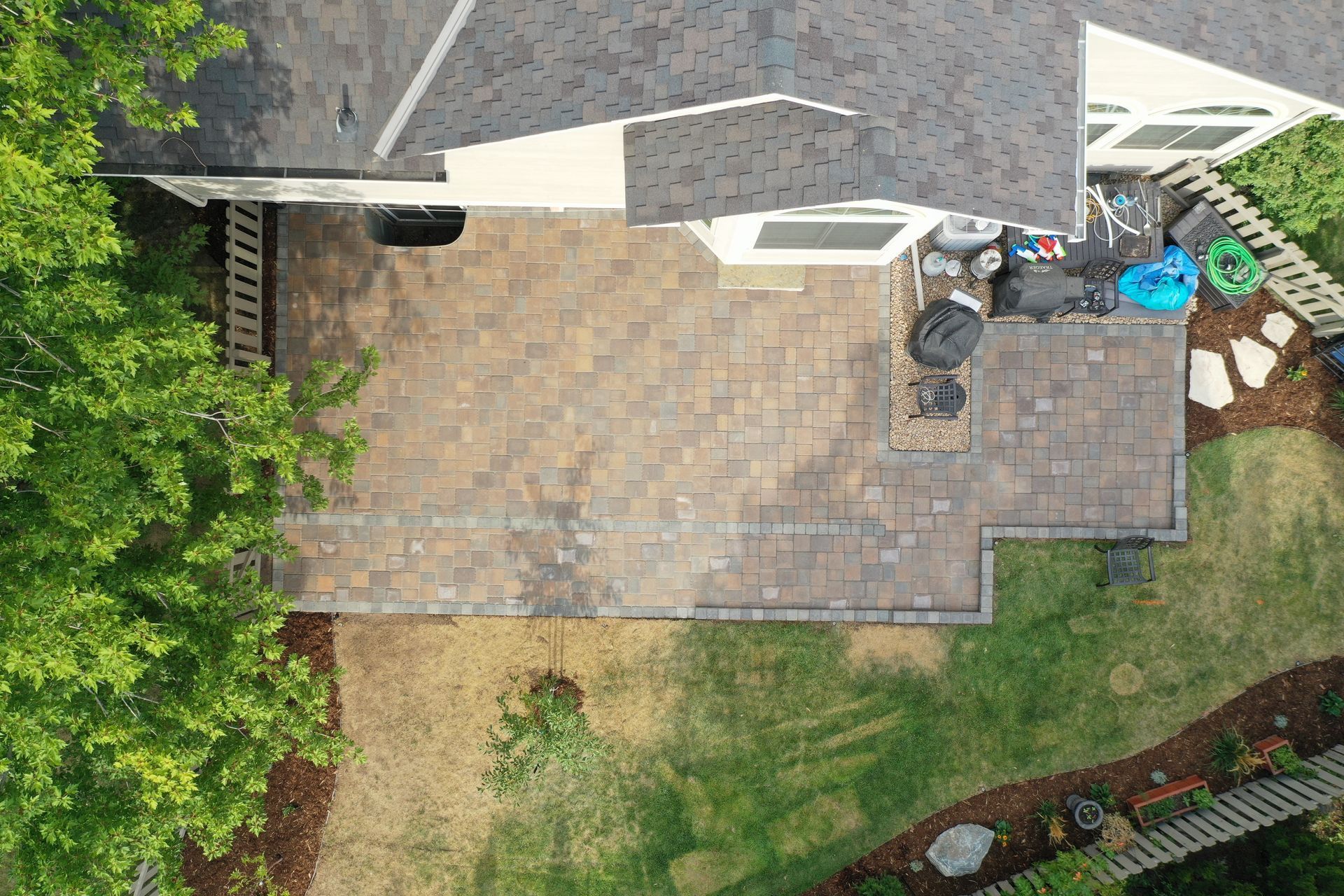 Overhead view of a house with a brick patio, green lawn, and surrounding trees.