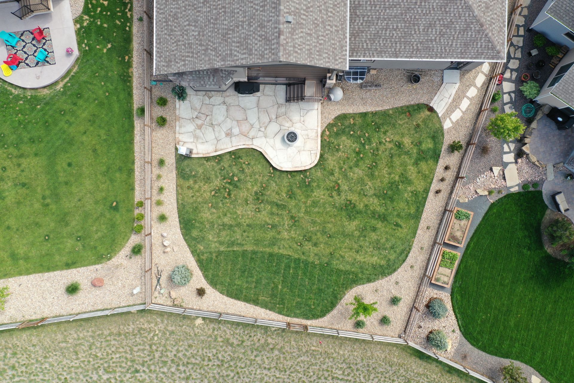 Aerial view of a backyard with a stone patio, green lawn, and landscaping surrounding a house.