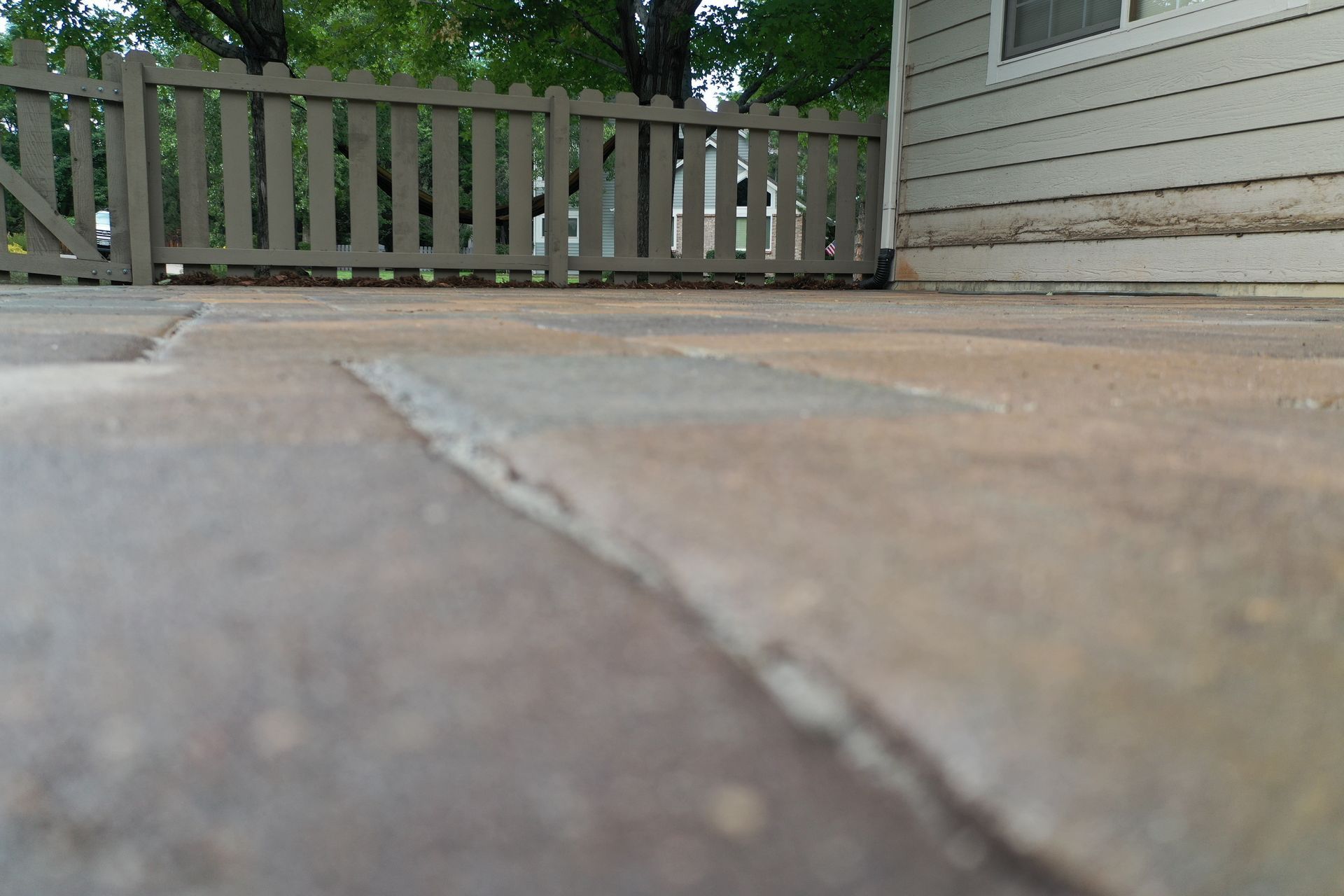 Close-up view of brick pavers with a wooden fence and house siding in the background.
