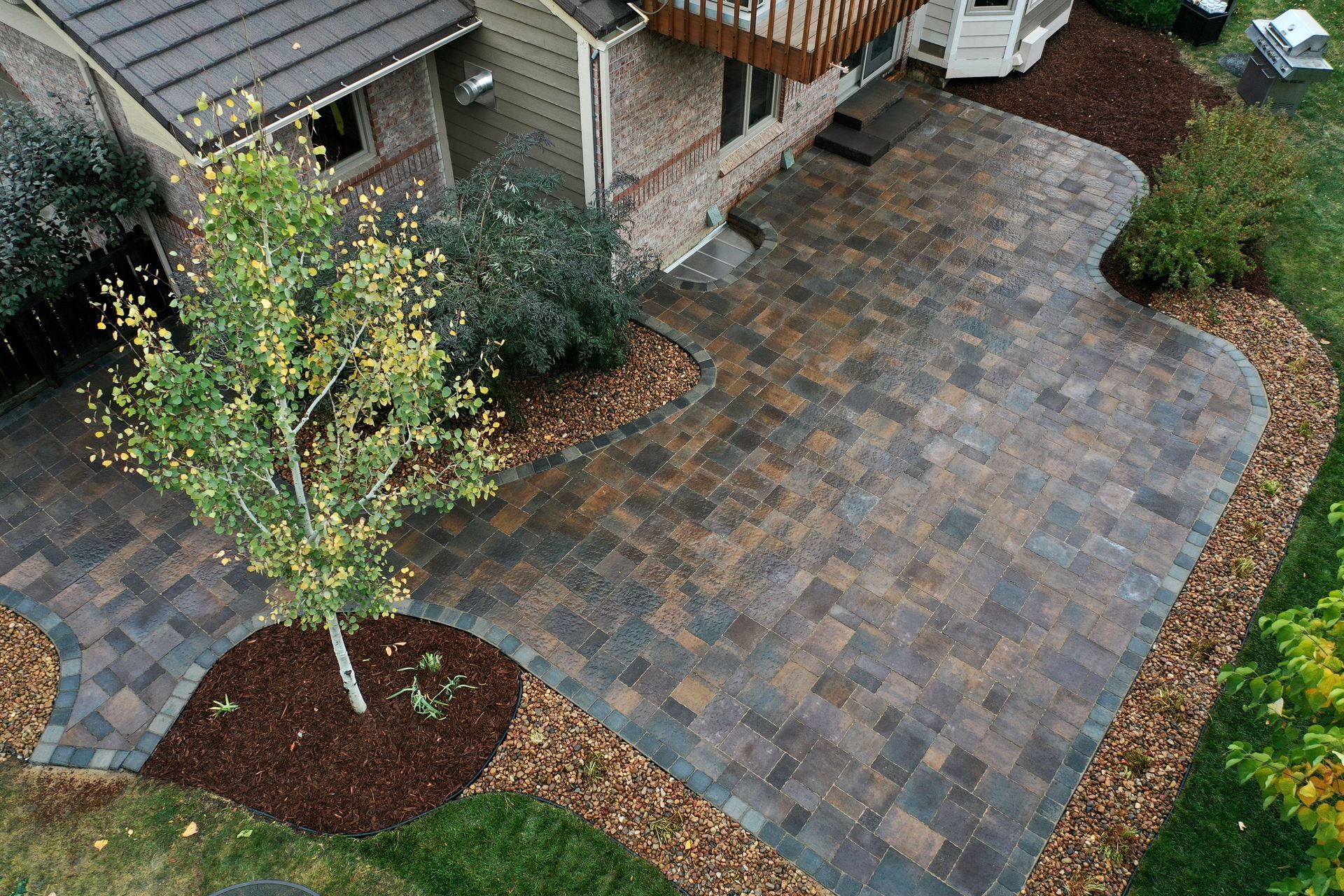 Overhead view of a brick patio with a tree, house, and landscaped yard.