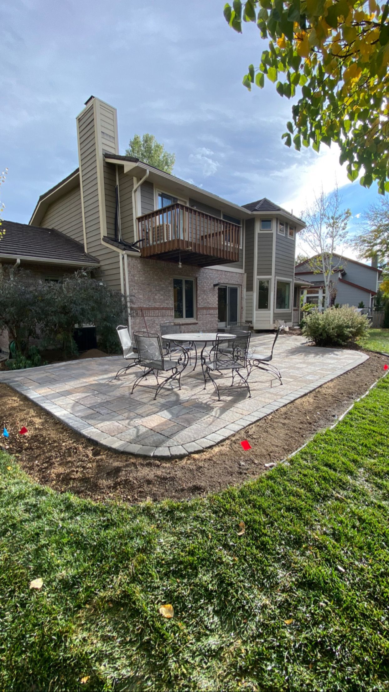 Backyard patio with a brick house, table, chairs, and grass.