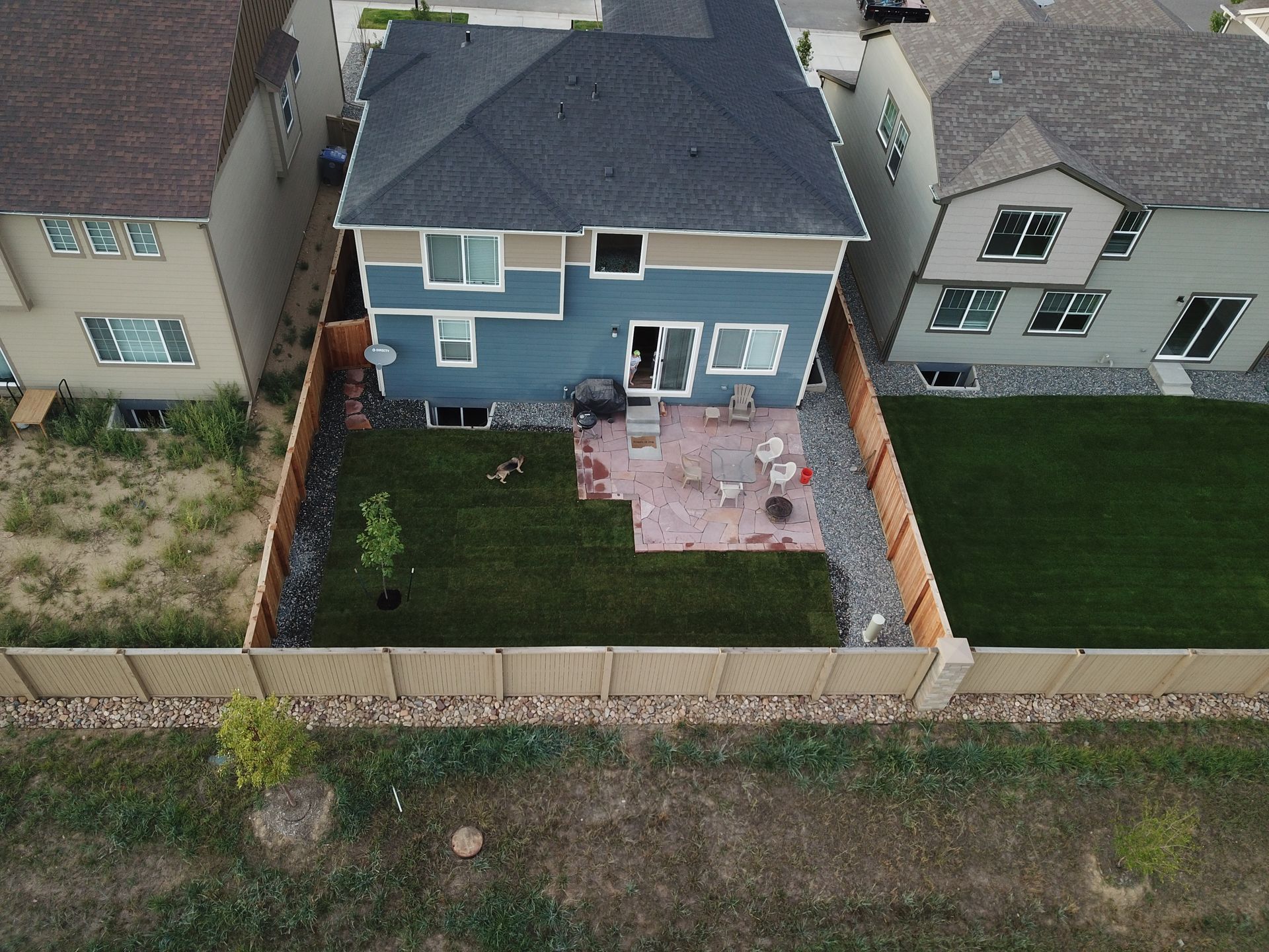 Aerial view of a blue two-story house with a backyard patio, surrounded by a wooden fence and neighboring houses.