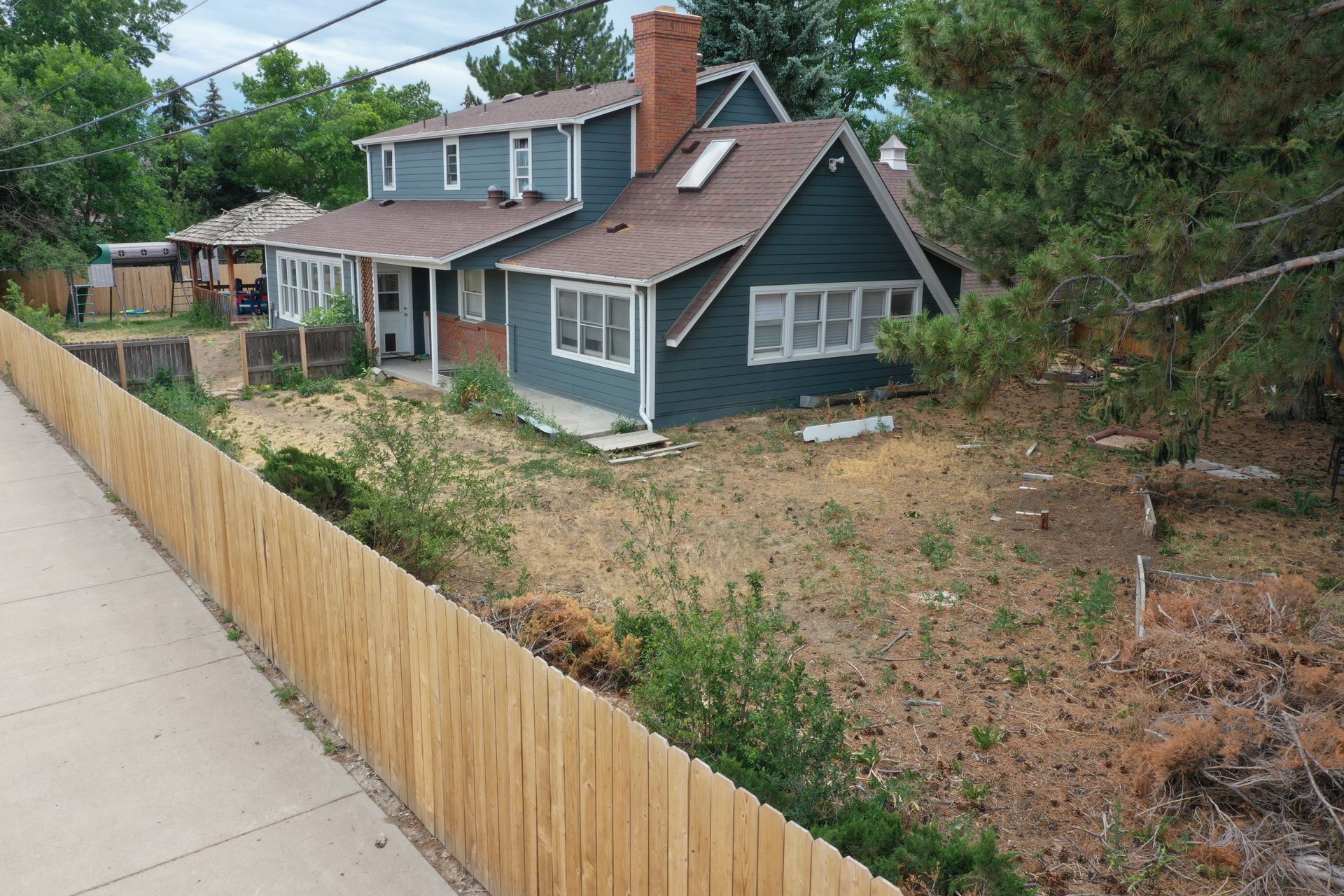 Blue two-story house with brown roof and wooden fence in front yard.
