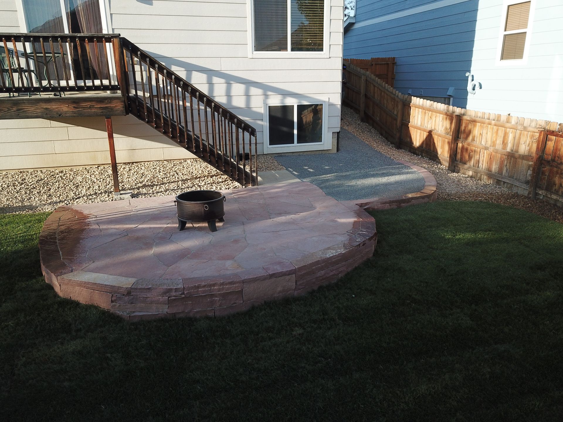 Backyard patio with fire pit, wooden stairs leading to a deck, and a grass lawn.