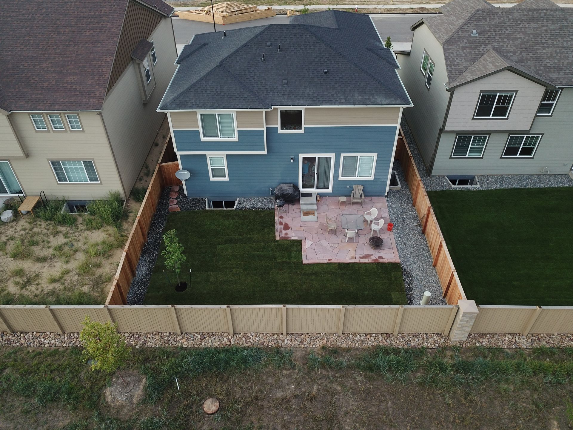 Aerial view of a two-story blue house with a fenced backyard, patio, and green lawn.