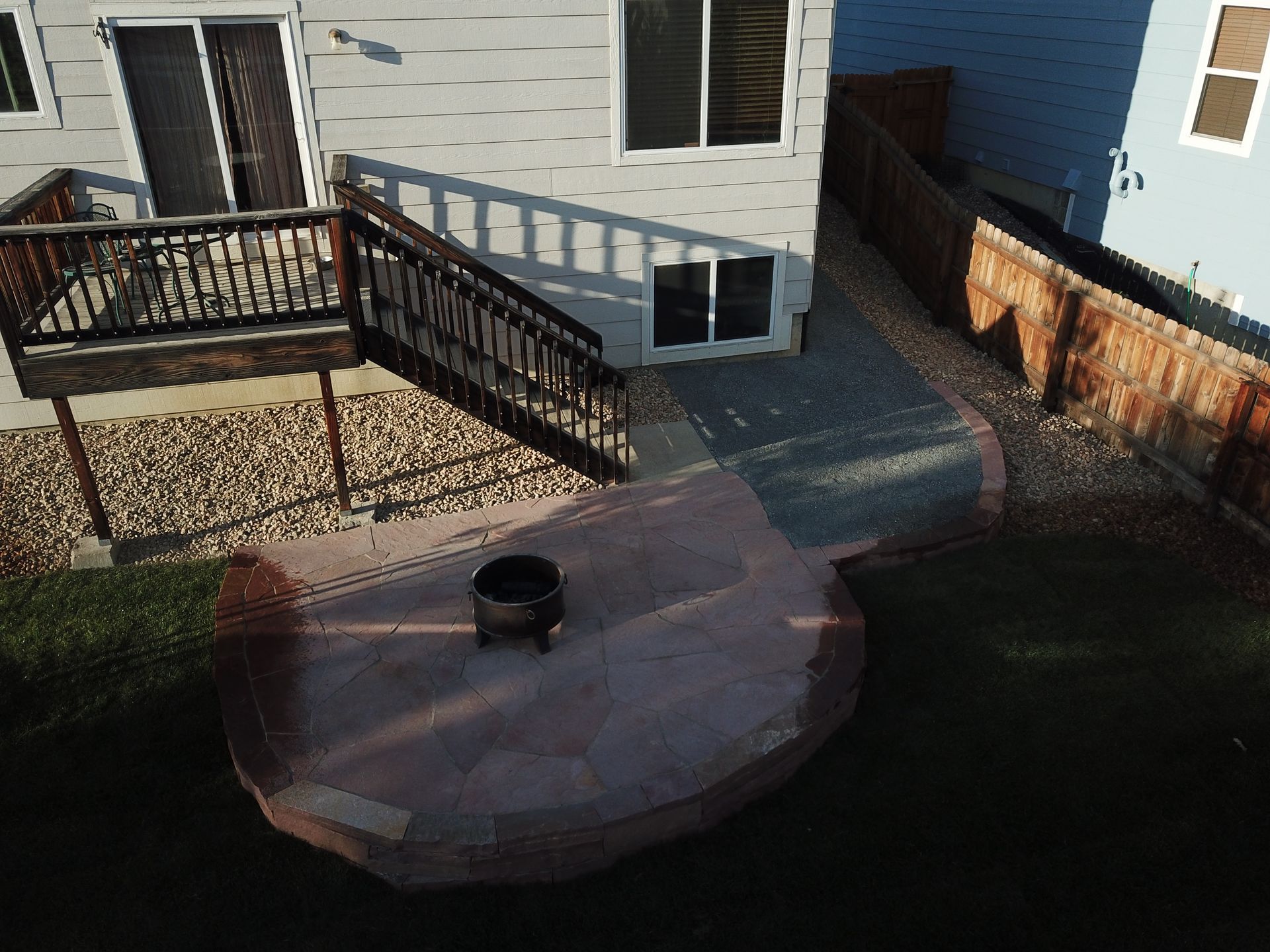 Backyard with a deck, patio, and fire pit next to a house with a blue exterior and brown fence.