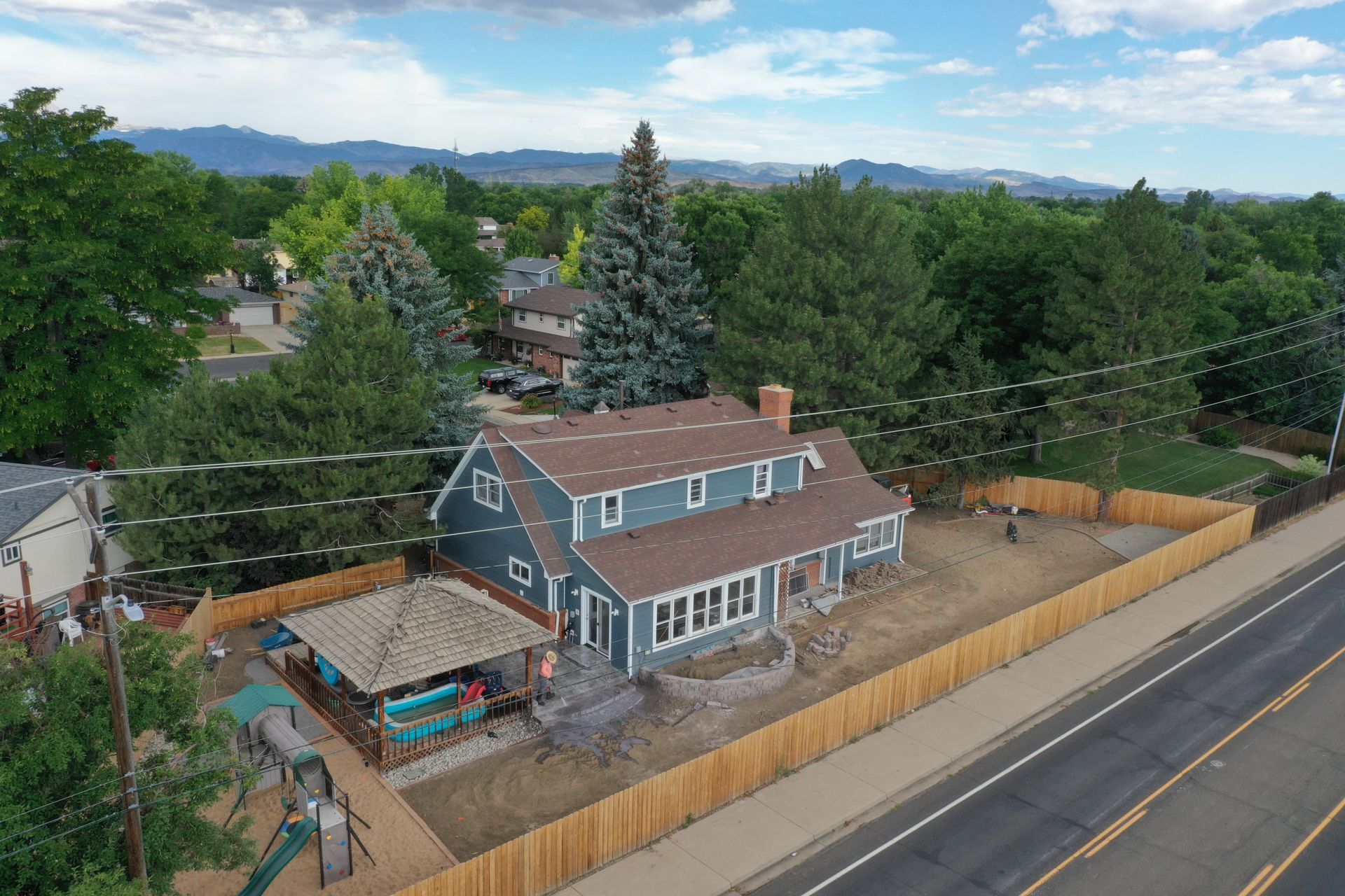 Aerial view of a blue-gray house with a wooden fence and mountain backdrop.