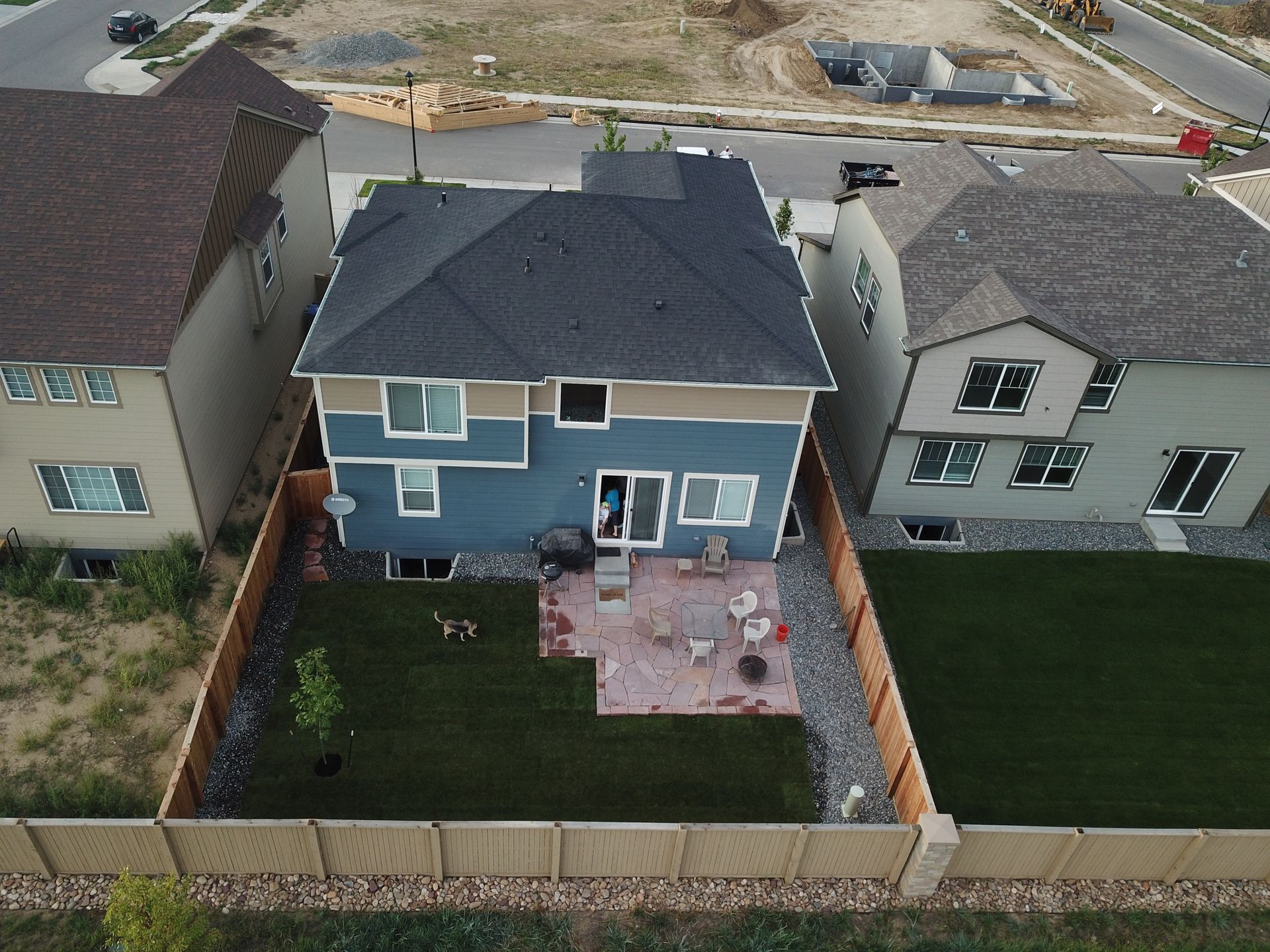 An aerial view of a blue two-story house with a backyard patio, lawn, and wooden fence.