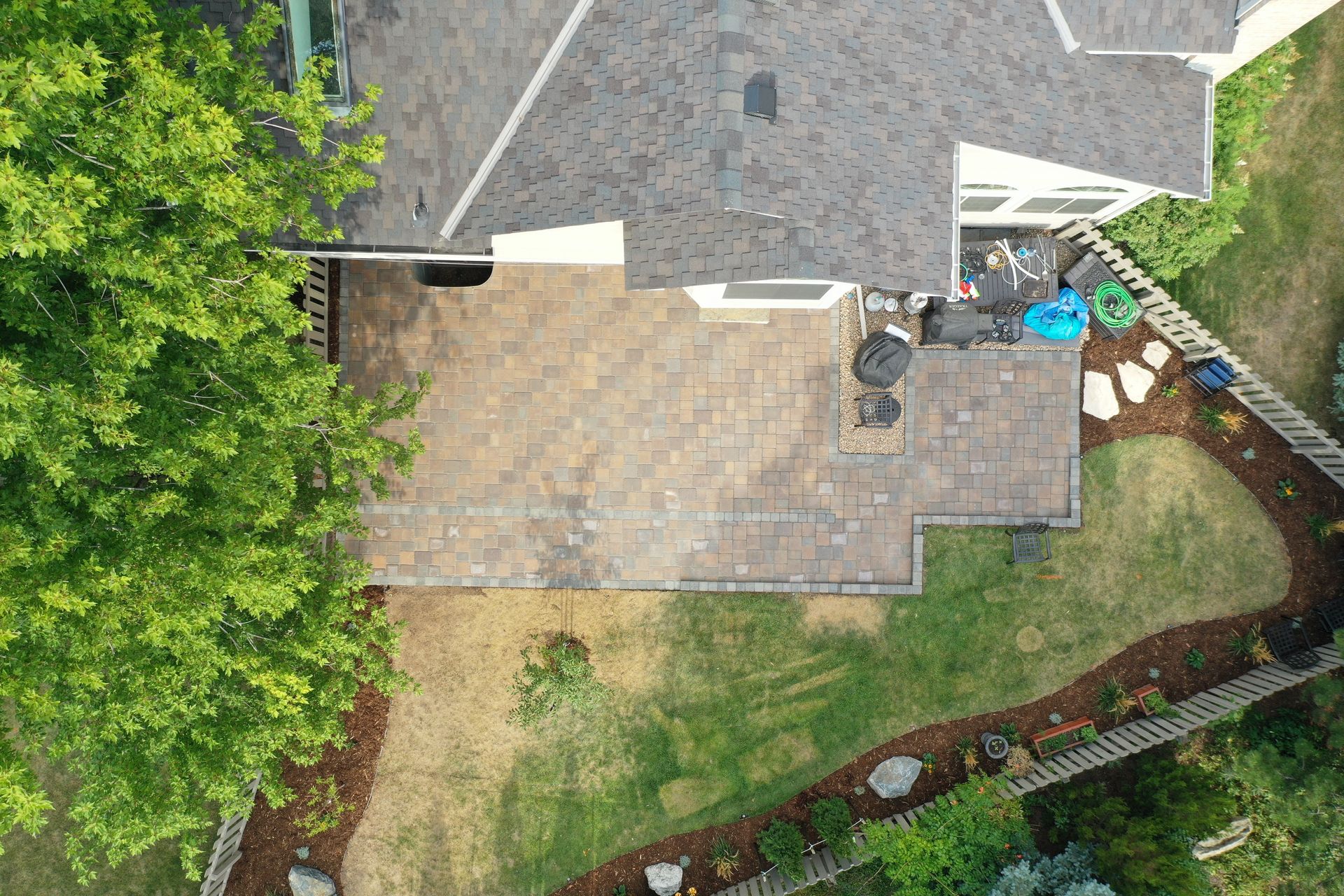 Overhead view of a house with a stone patio, a green lawn, and a fence bordering the yard.