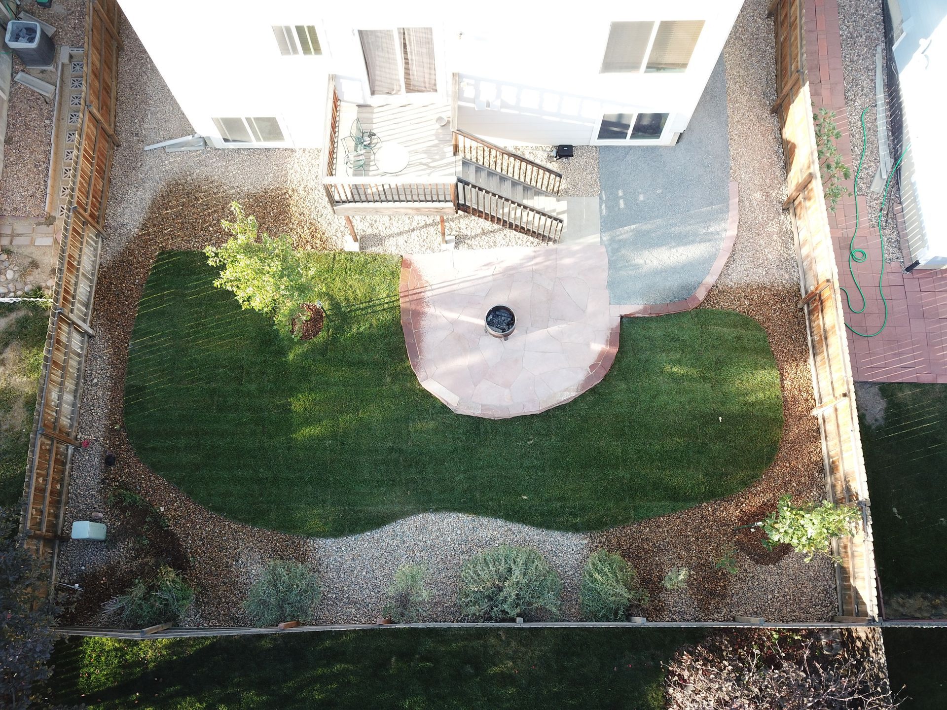 Overhead view of a backyard with a grass area, fire pit, patio, and surrounding landscaping.