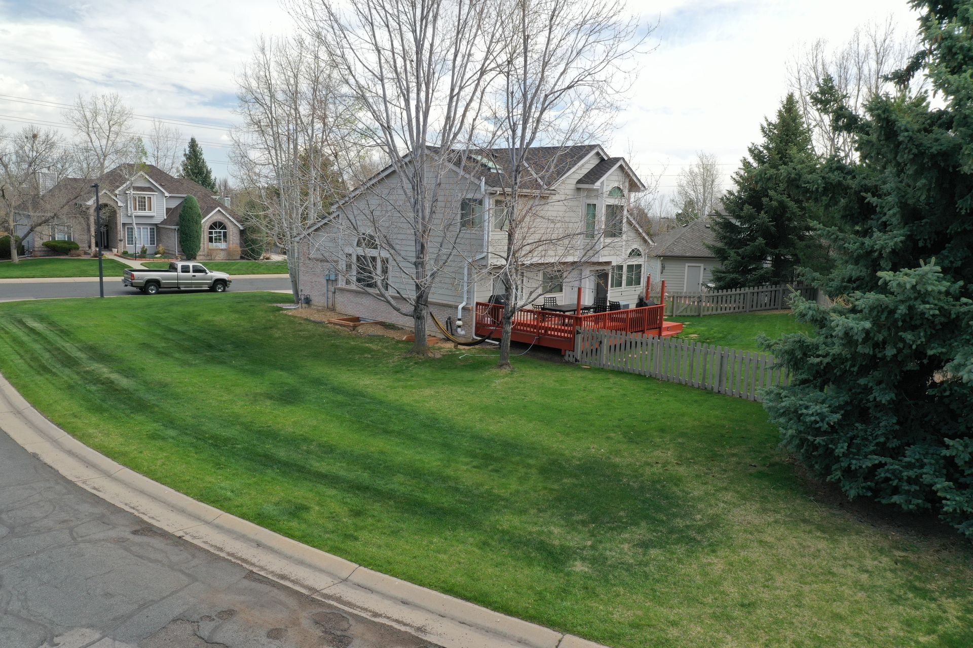 Two-story house with green lawn, trees, and a truck parked on the street.