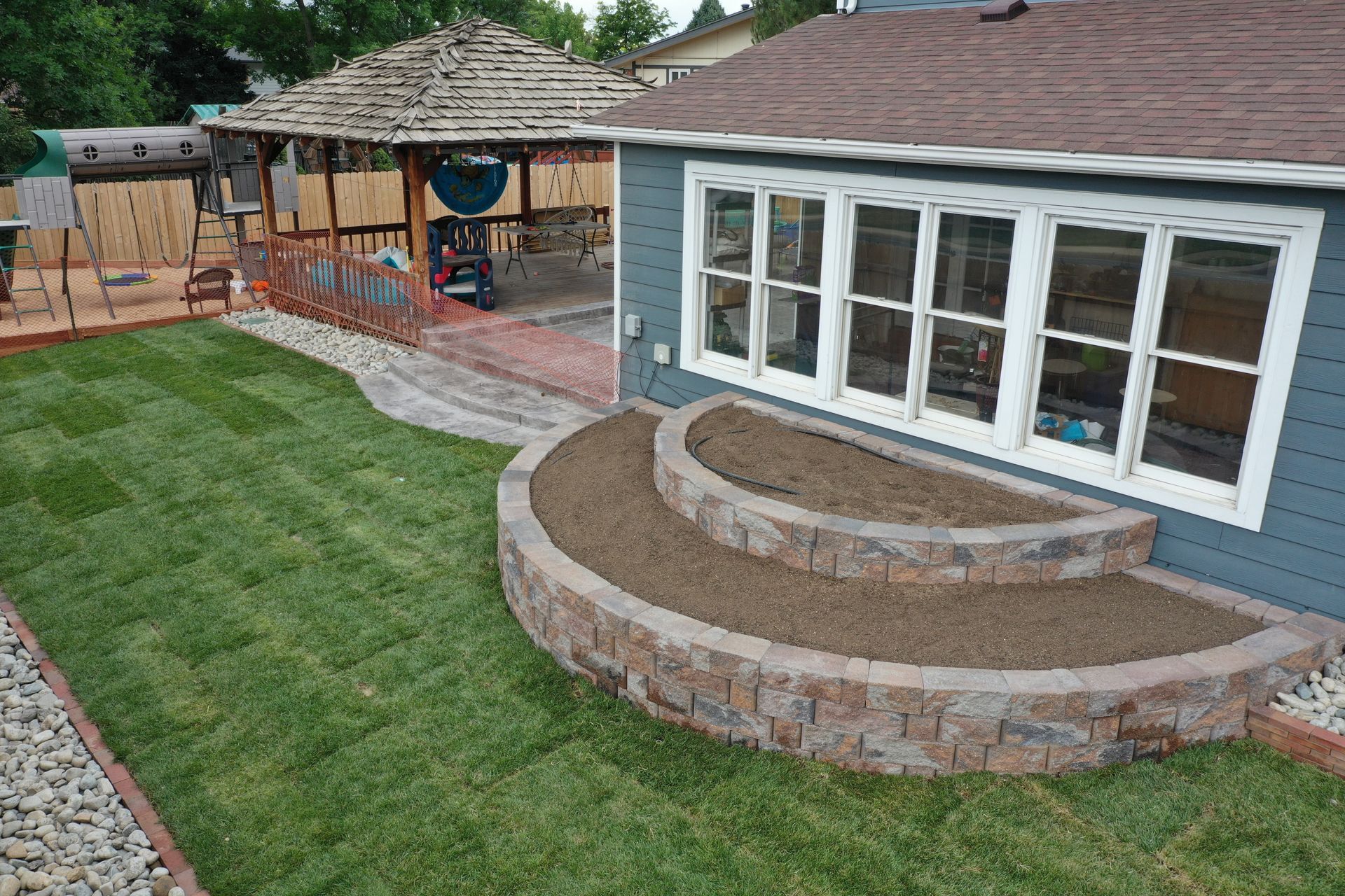 Backyard with gazebo, steps, and house with large windows; green lawn.