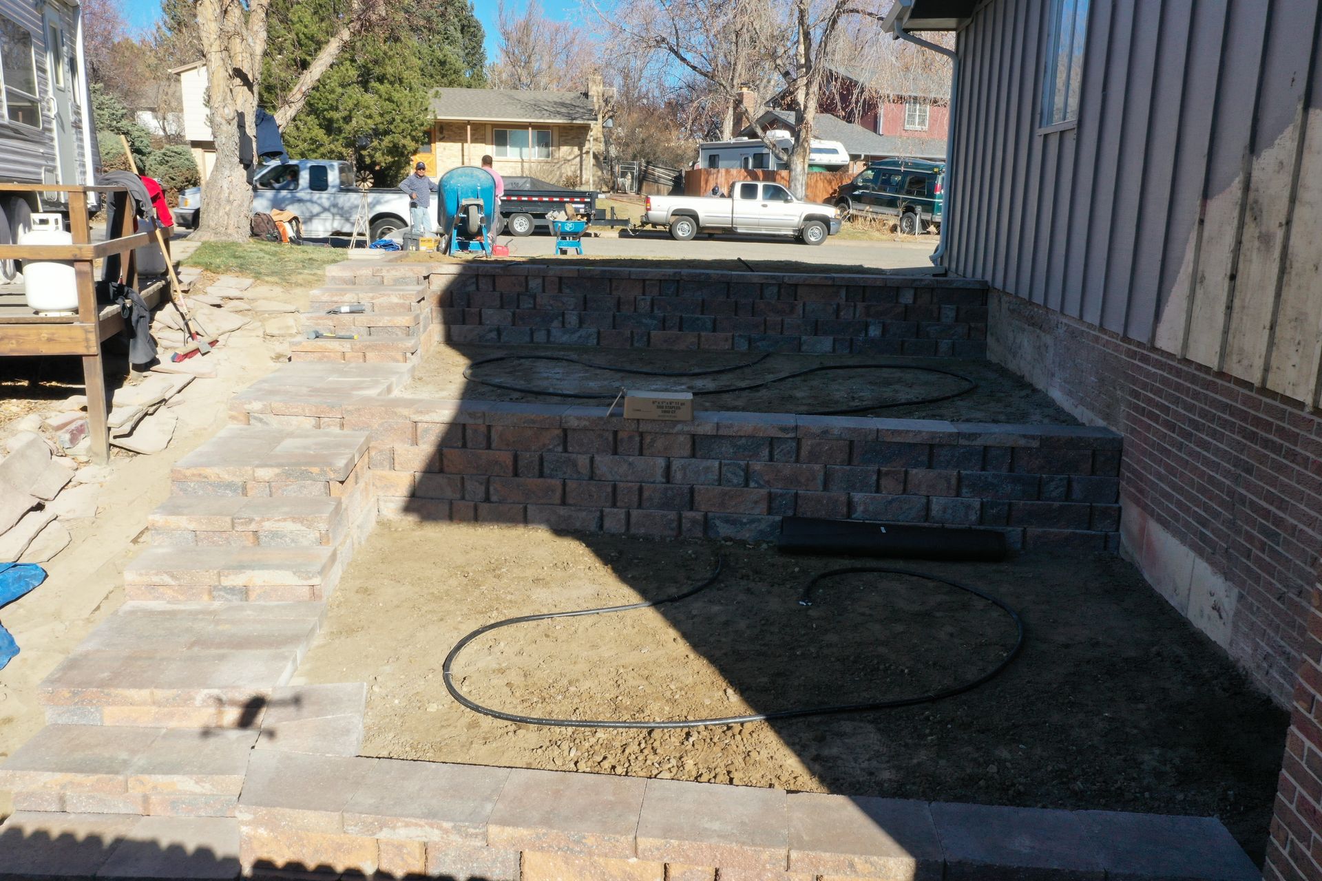 A brick retaining wall and steps being built next to a building. Construction equipment and trucks in the background.